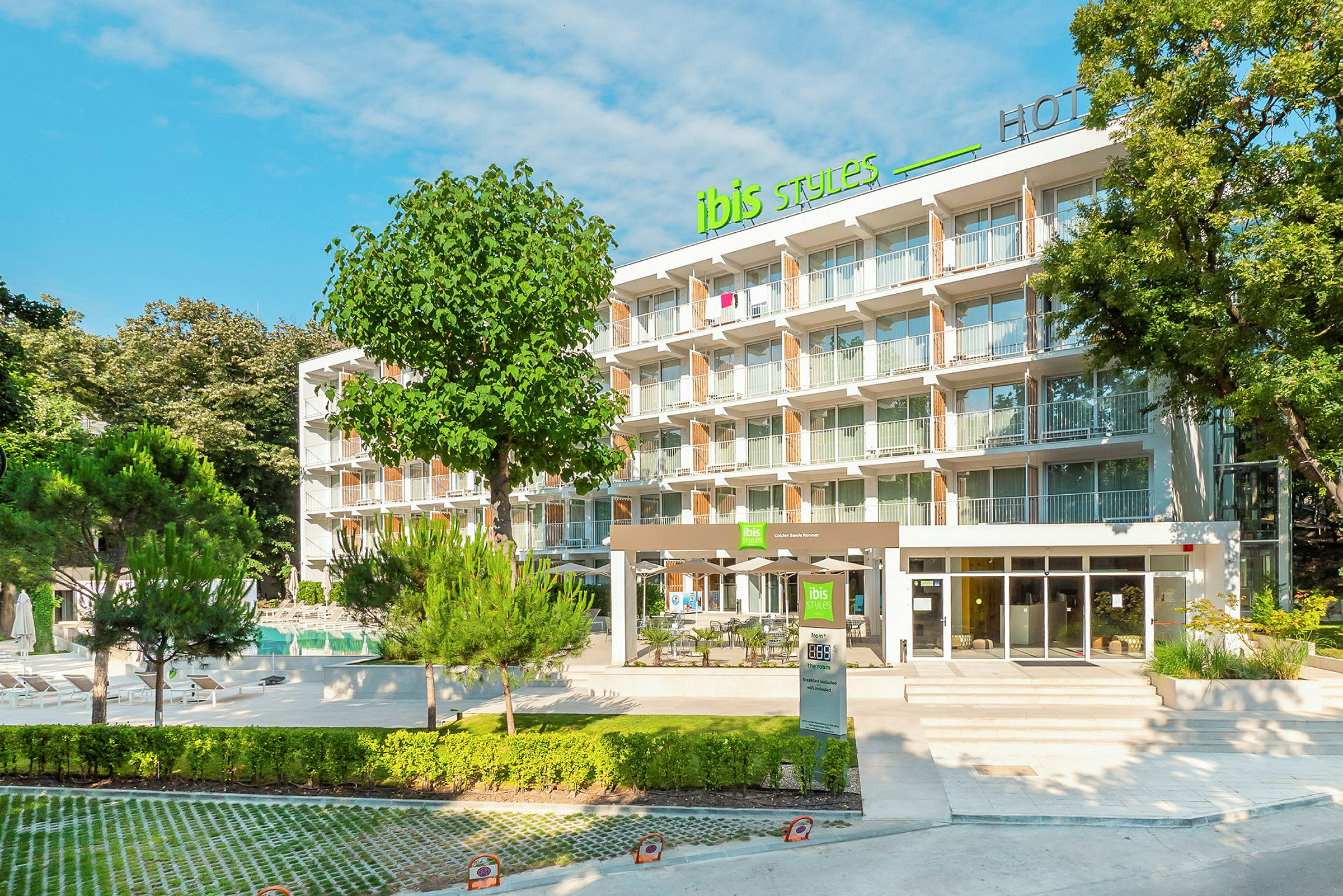 Hotellbyggnad med en modern fasad och flera våningar omringad av grönska och träd. (AI-genererad text)