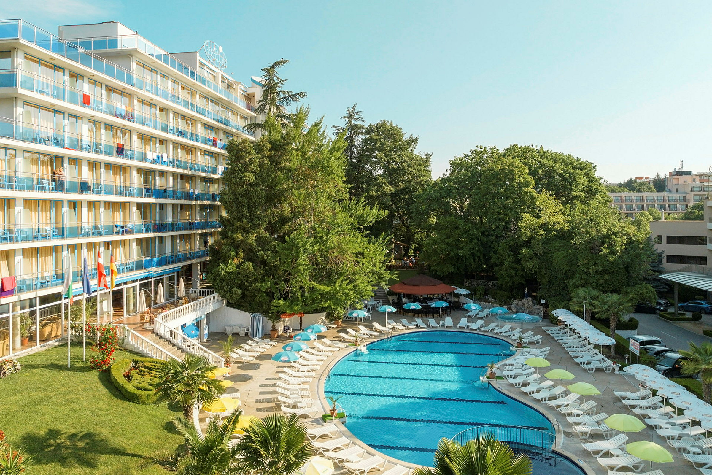 Hotellbyggnad med balkonger och poolområde omgiven av solstolar och parasoller. (AI-genererad text)