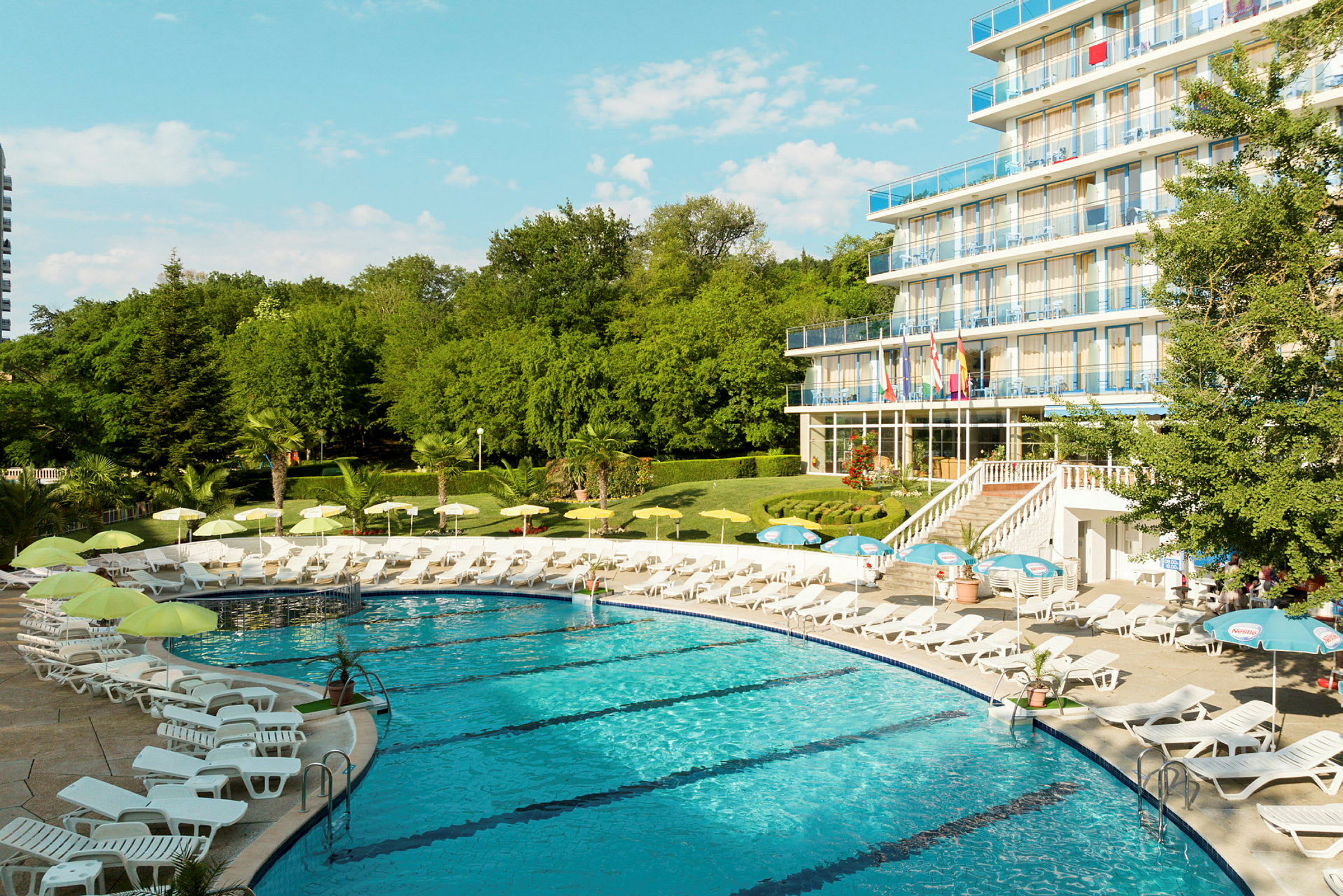 En pool omgiven av solstolar och parasoller nära ett hotell med flera våningar. (AI-genererad text)