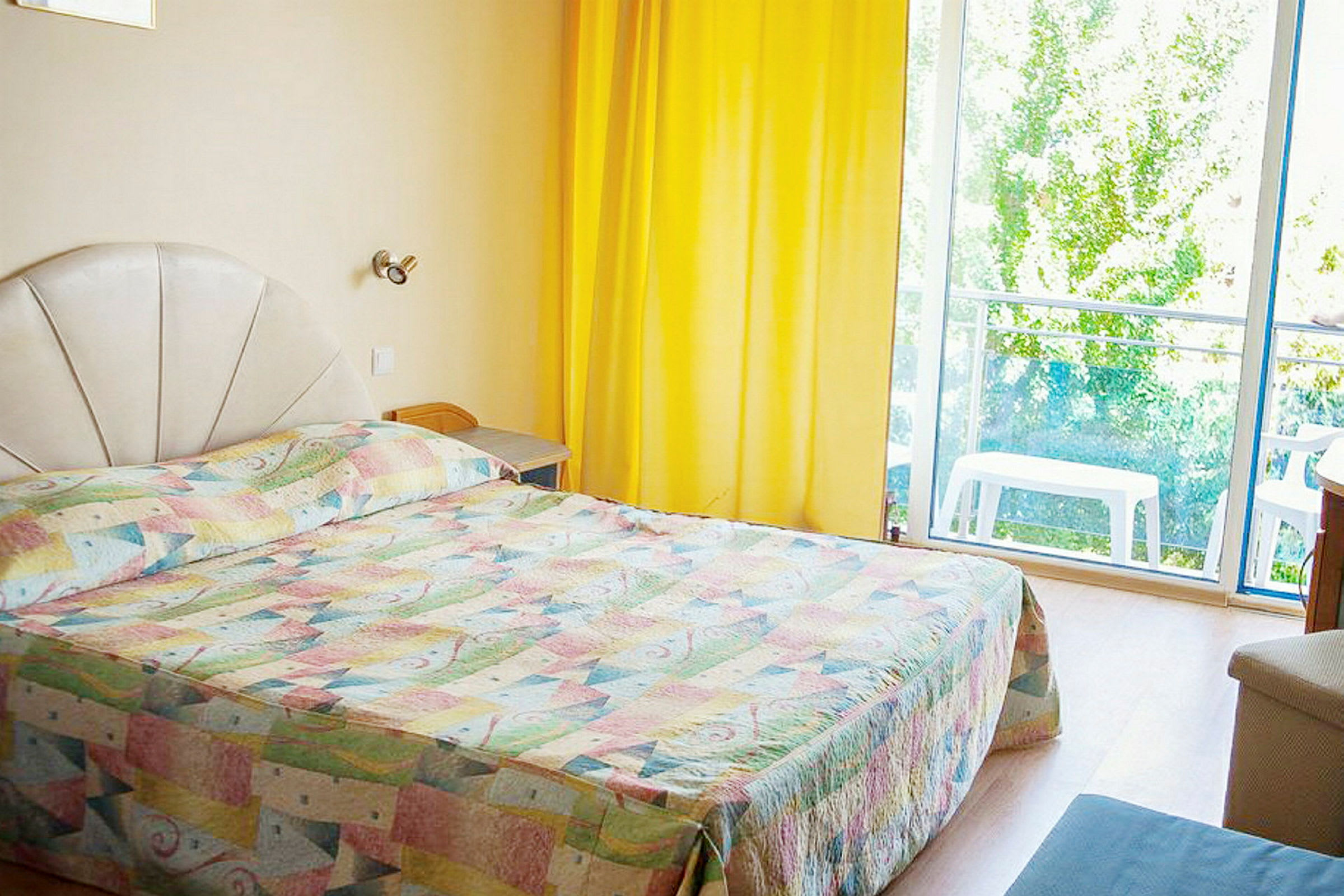 En hotellrum med en säng, gula gardiner och ett fönster med utsikt. (AI-genererad text)