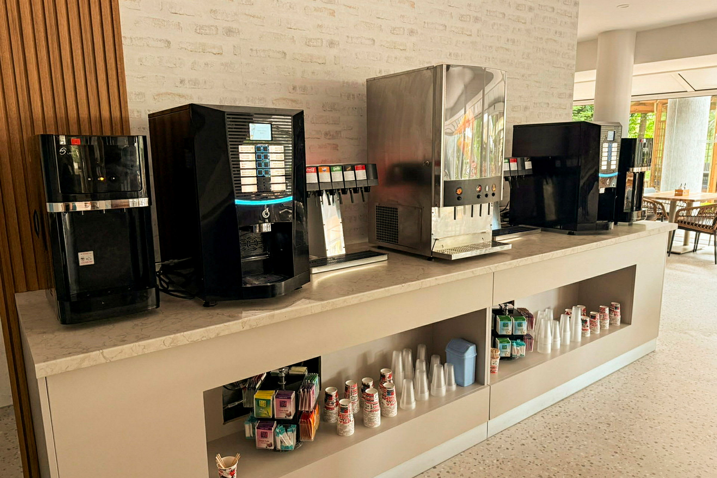 Bilden visar en dryckesstation med flera automater och tillhörande tillbehör som koppar och sugrör. (AI-genererad text)