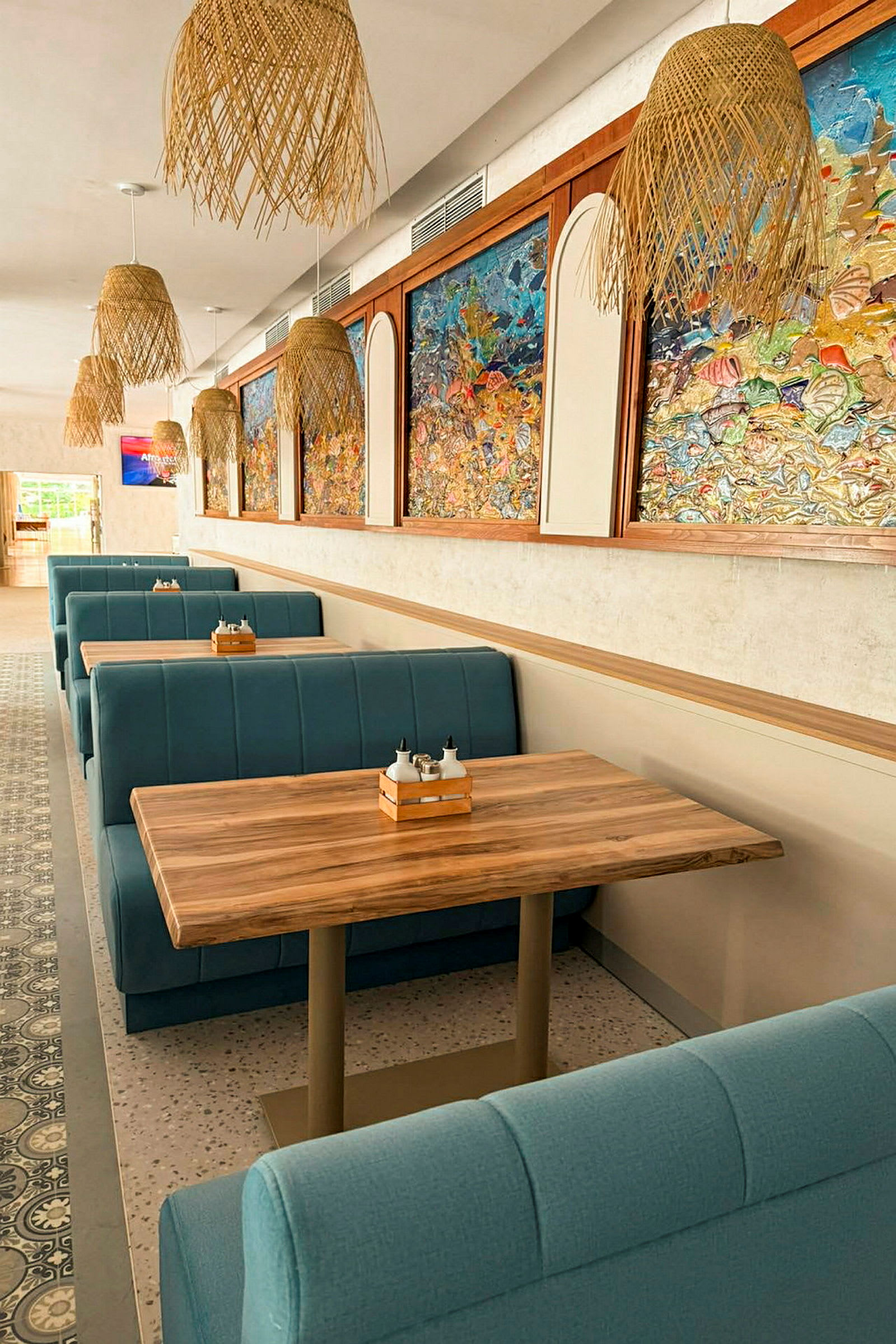Bild av en restaurang med blå bås och träbord. Väggarna är dekorerade med färgstarka konstverk och taket har flätade lampor. (AI-genererad text)