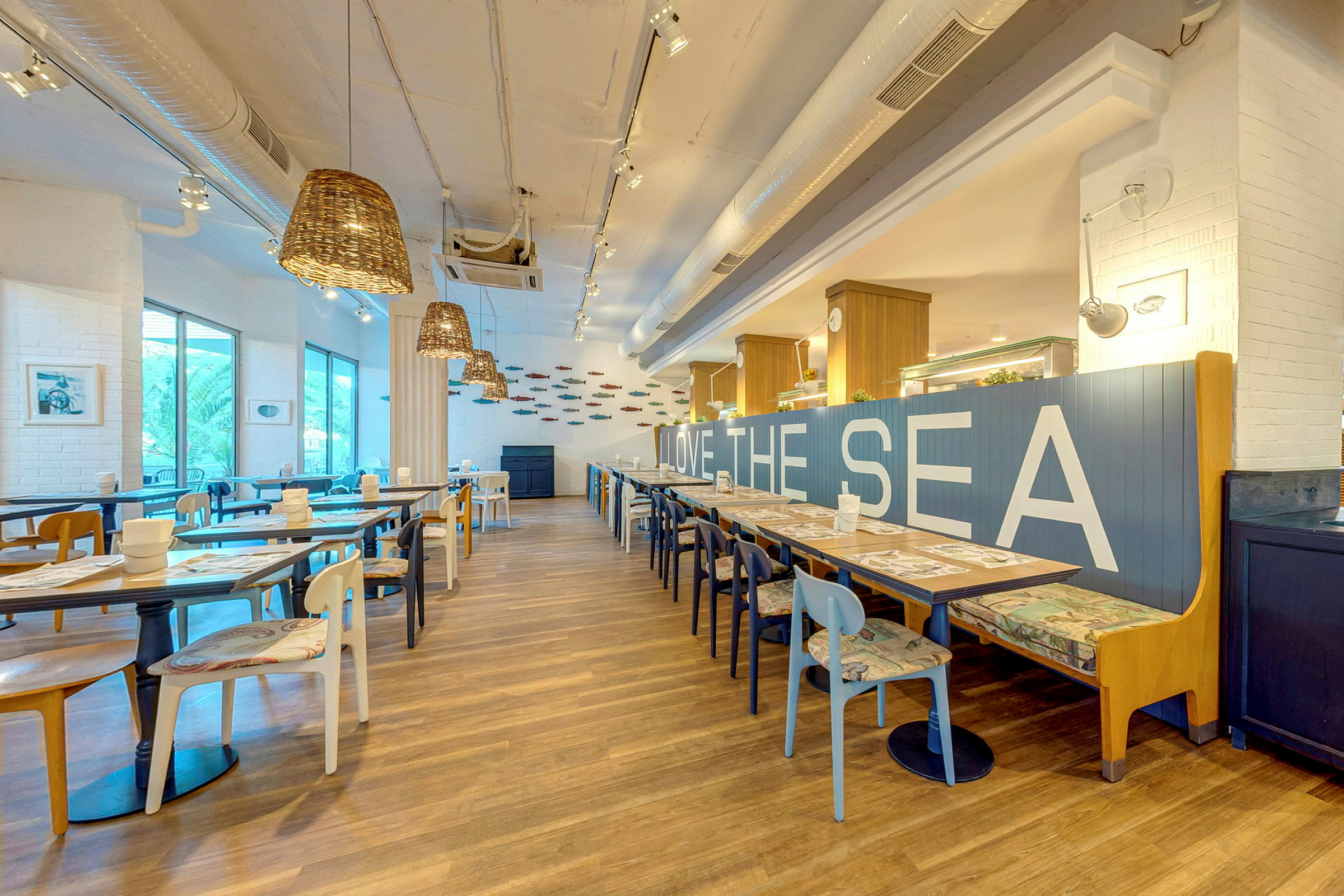 En modern restaurang med ljus inredning, träbord och stolar, samt texten 'LOVE THE SEA' på ett blått ryggstöd. (AI-genererad text)