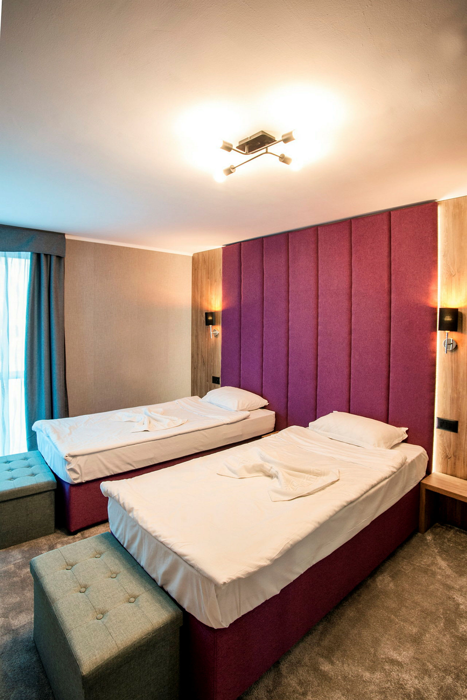 Ett hotellrum med två enkelsängar, en lila huvudgavel och inredning i modern stil. (AI-genererad text)