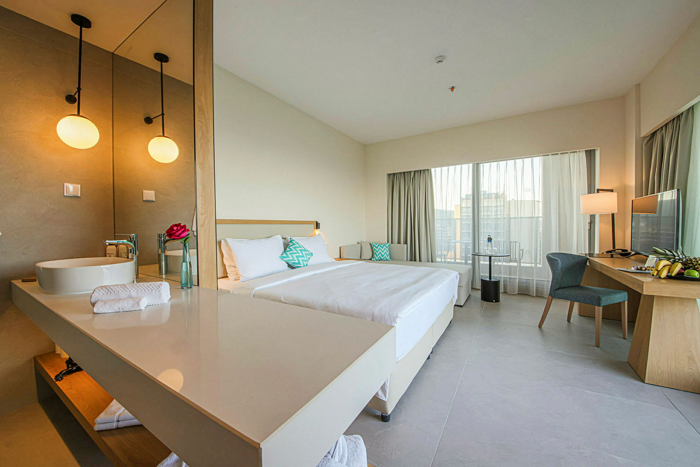 Ett hotellrum med en dubbelsäng, ett skrivbord med stol och en stor spegel vid handfatet. (AI-genererad text)