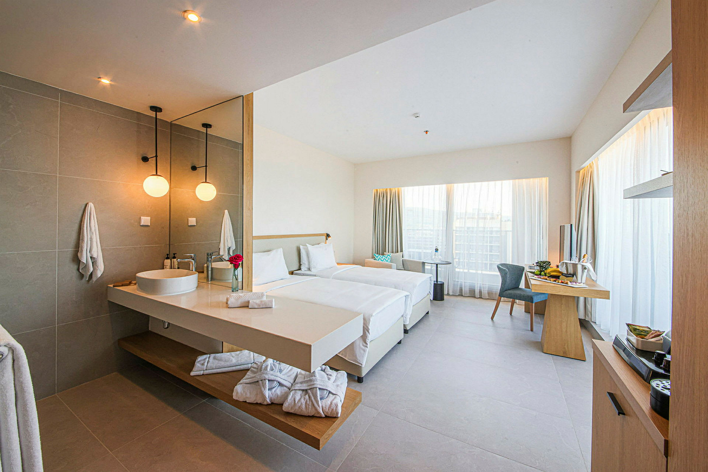 Ett modernt hotellrum med två enkelsängar, skrivbord och integrerat badrum med handfat. (AI-genererad text)