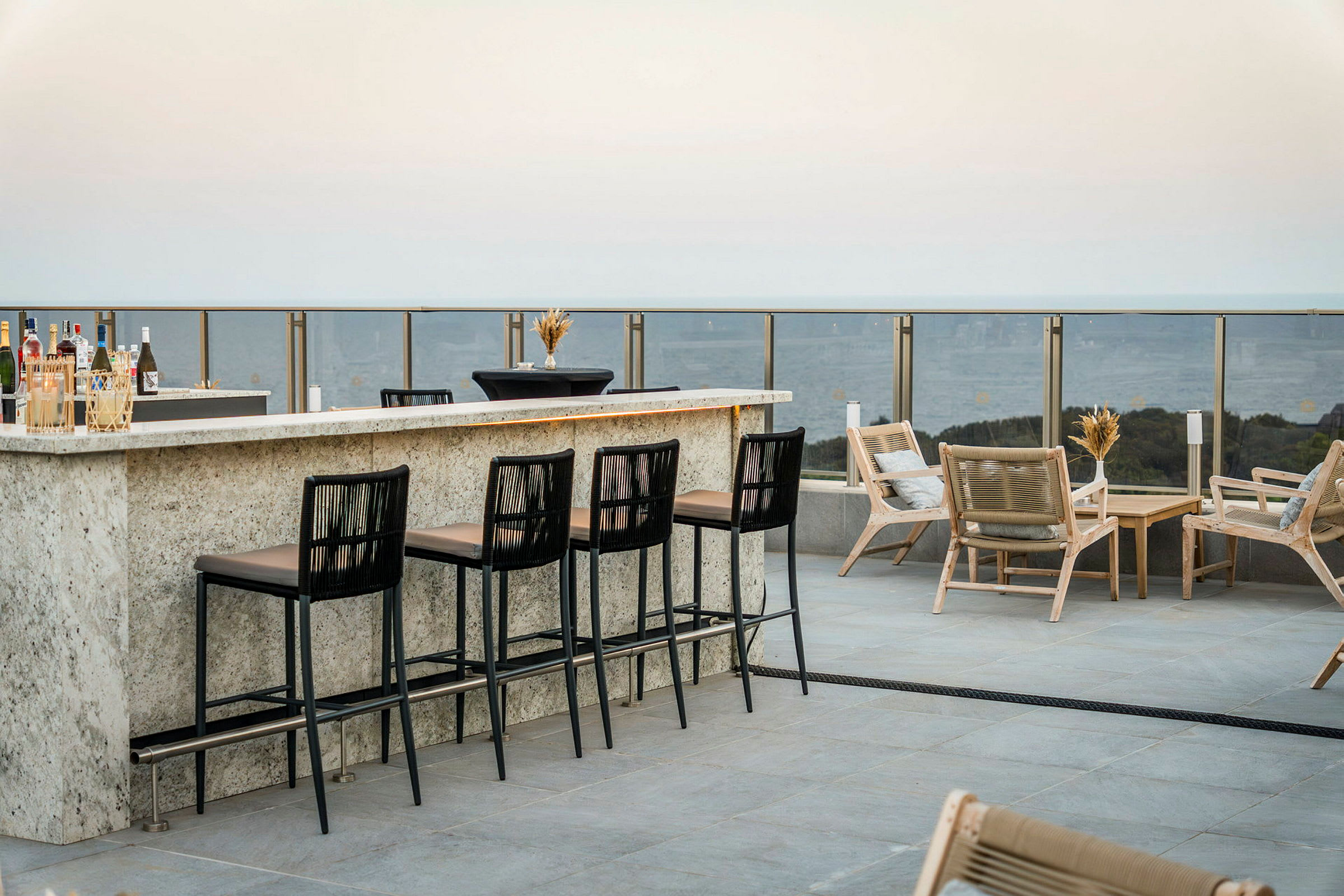 En utomhusbar med höga stolar och loungemöbler på en terrass med utsikt. (AI-genererad text)