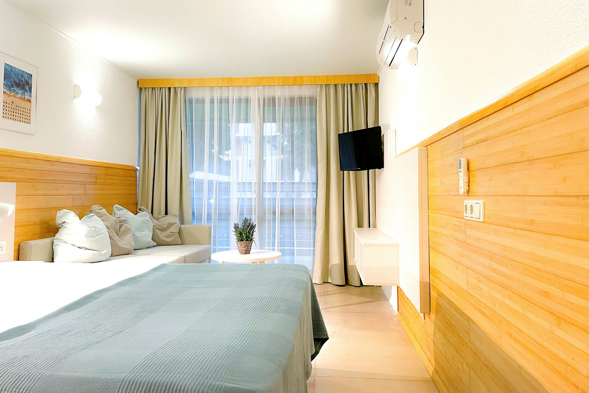 Ett hotellrum med säng, soffa och bord. Gardiner hänger framför en stor fönsteryta. (AI-genererad text)