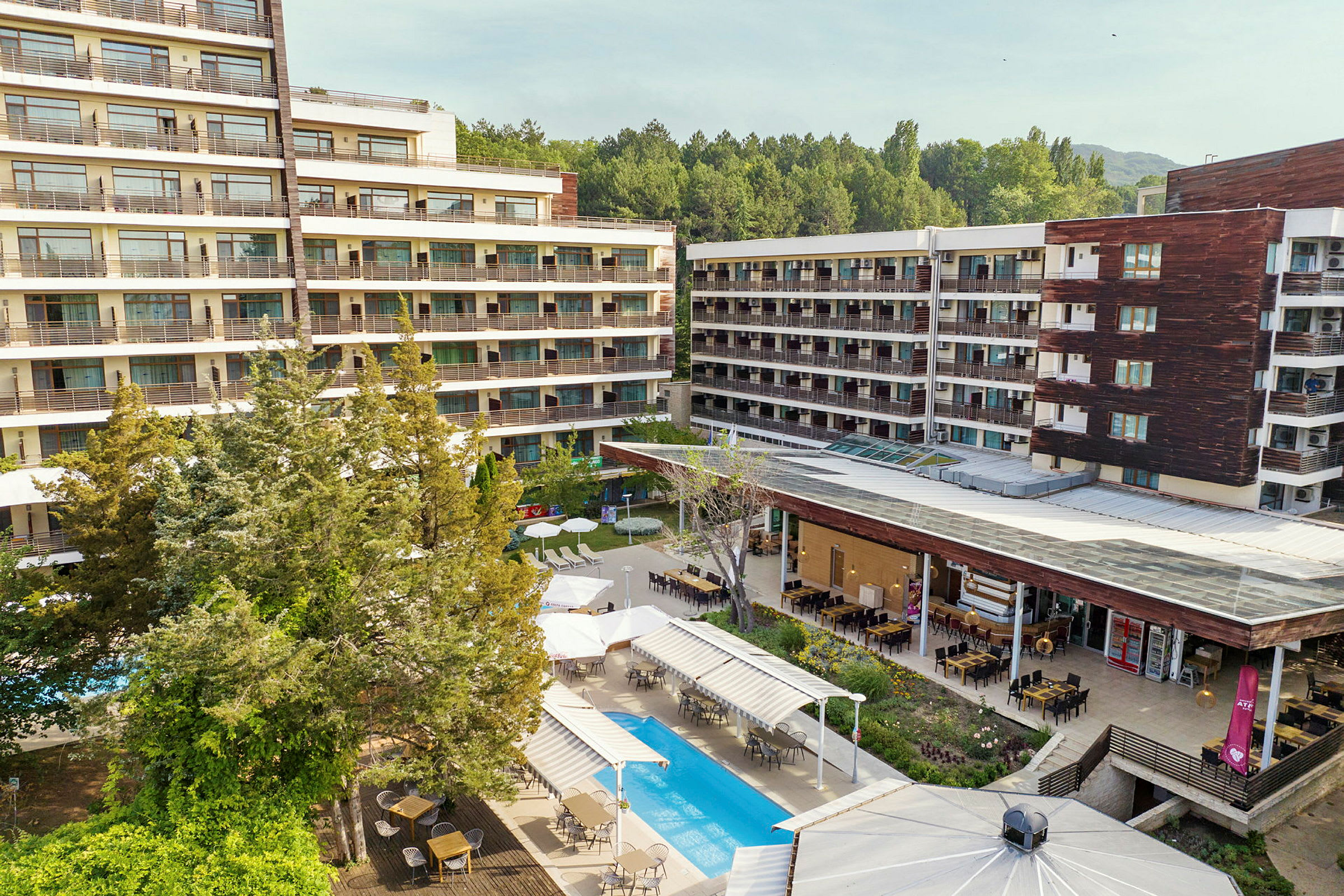Hotellbyggnader omgivna av grönska. Pool och utomhusmatplats syns i förgrunden. (AI-genererad text)