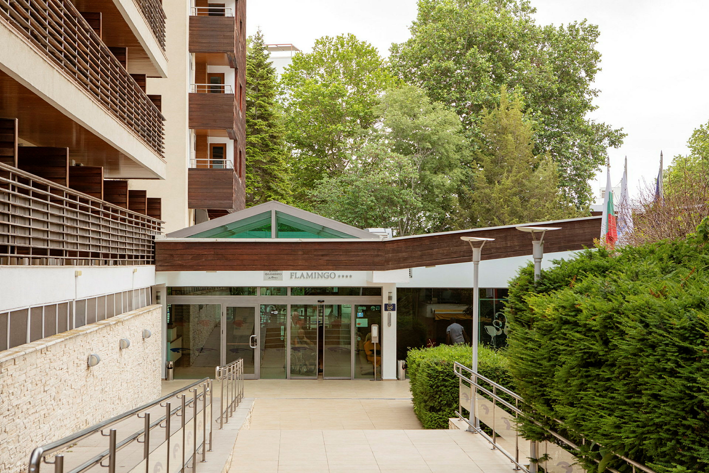 Hotellentré med glasdörrar och omgivande grönska. (AI-genererad text)