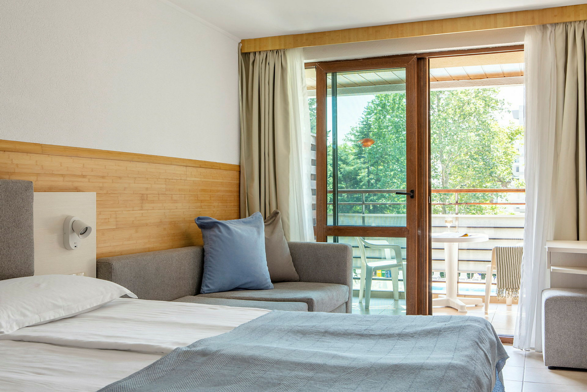 Ett hotellrum med en säng, soffa och balkongmöbler synliga genom en glasdörr. (AI-genererad text)