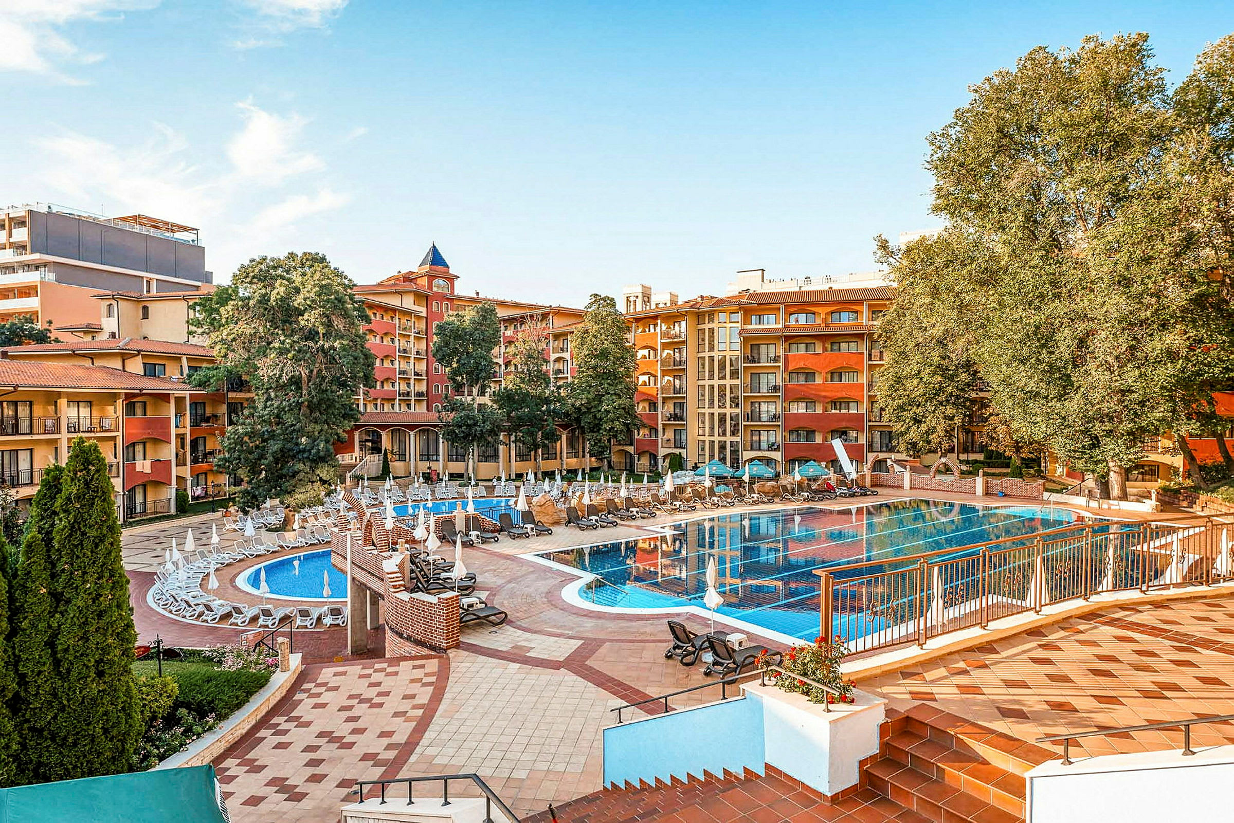 Hotellets poolområde med solstolar, parasoller och byggnader i bakgrunden. (AI-genererad text)