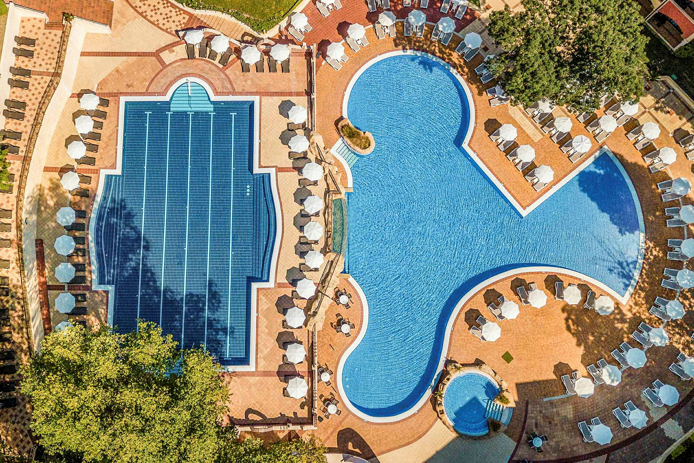 Flygfoto av två olika pooler med solstolar och parasoller runt omkring. (AI-genererad text)