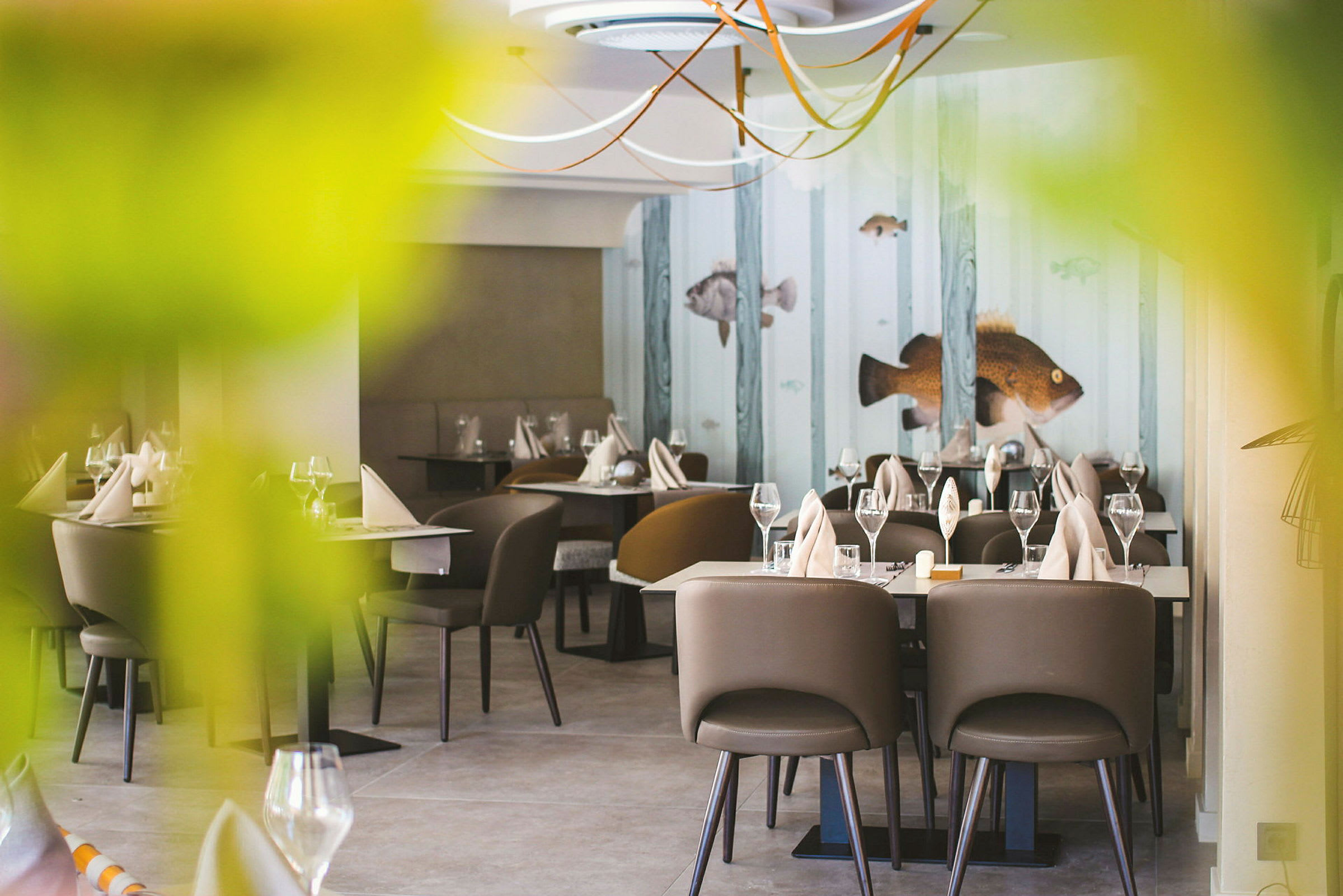 Restaurang med dukade bord, brunstolar och dekorationer med fiskmotiv på väggen. (AI-genererad text)