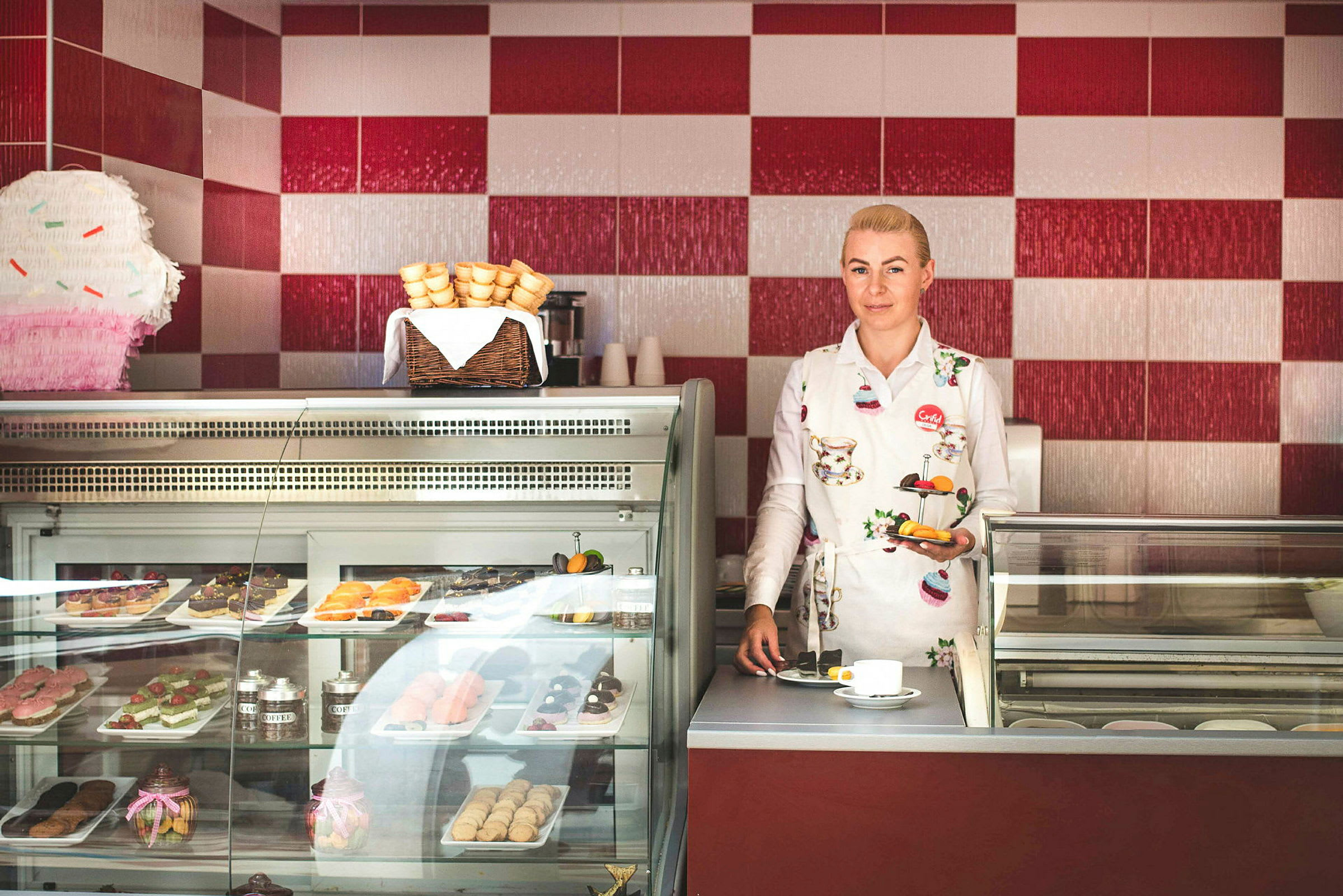 En person står bakom en glassdisk med bakverk i en butik. (AI-genererad text)