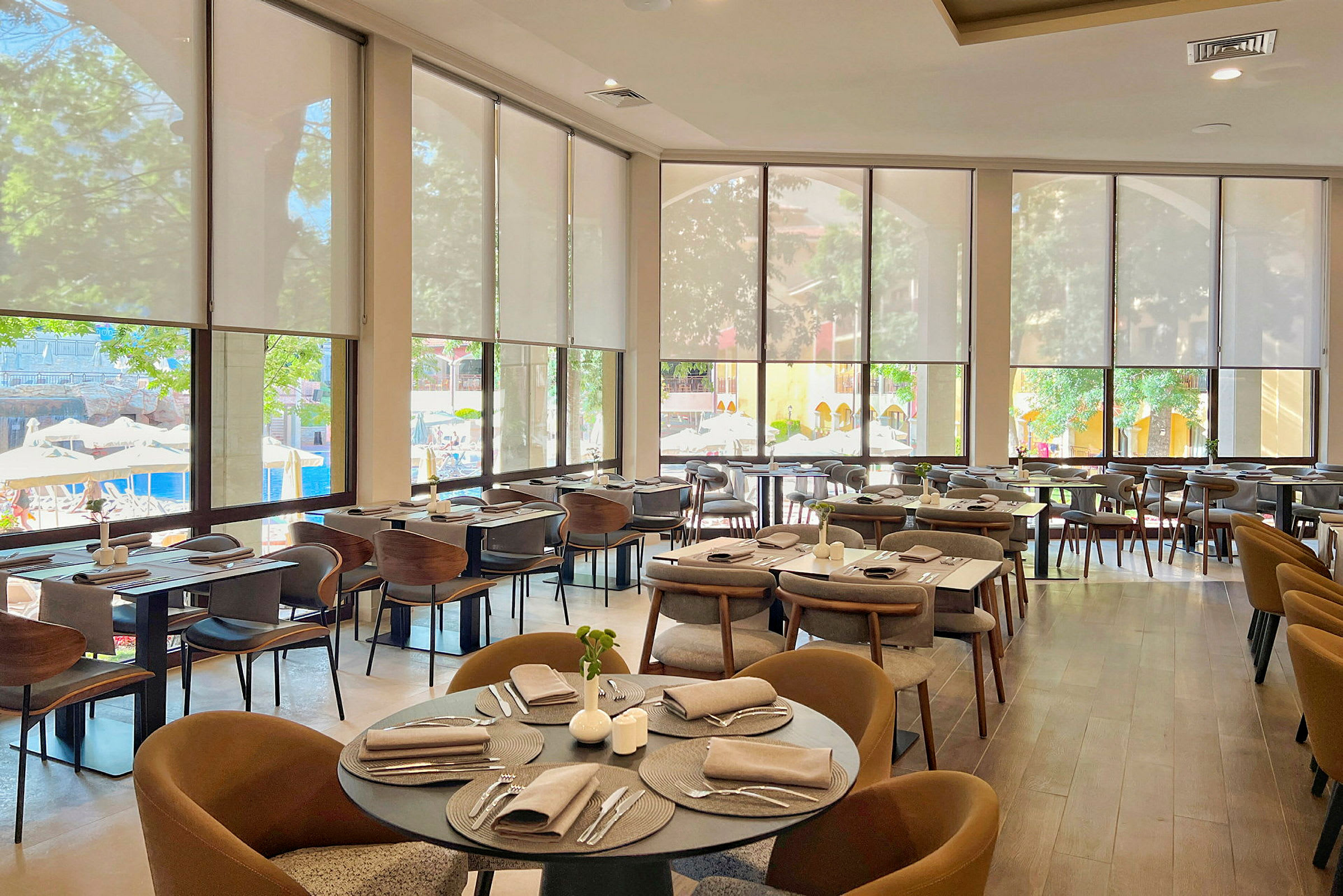 En restaurang med dukade bord och stora fönster som vetter mot en utomhuspool. (AI-genererad text)