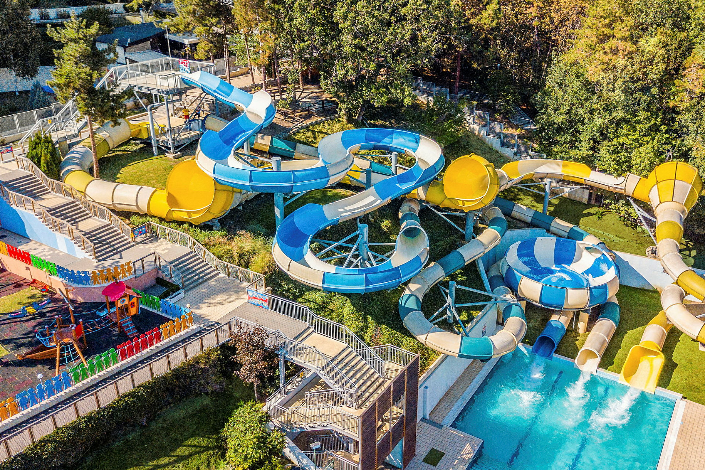 En aktivitetpark med vattenrutschkanor i olika färger och former bredvid en pool. (AI-genererad text)