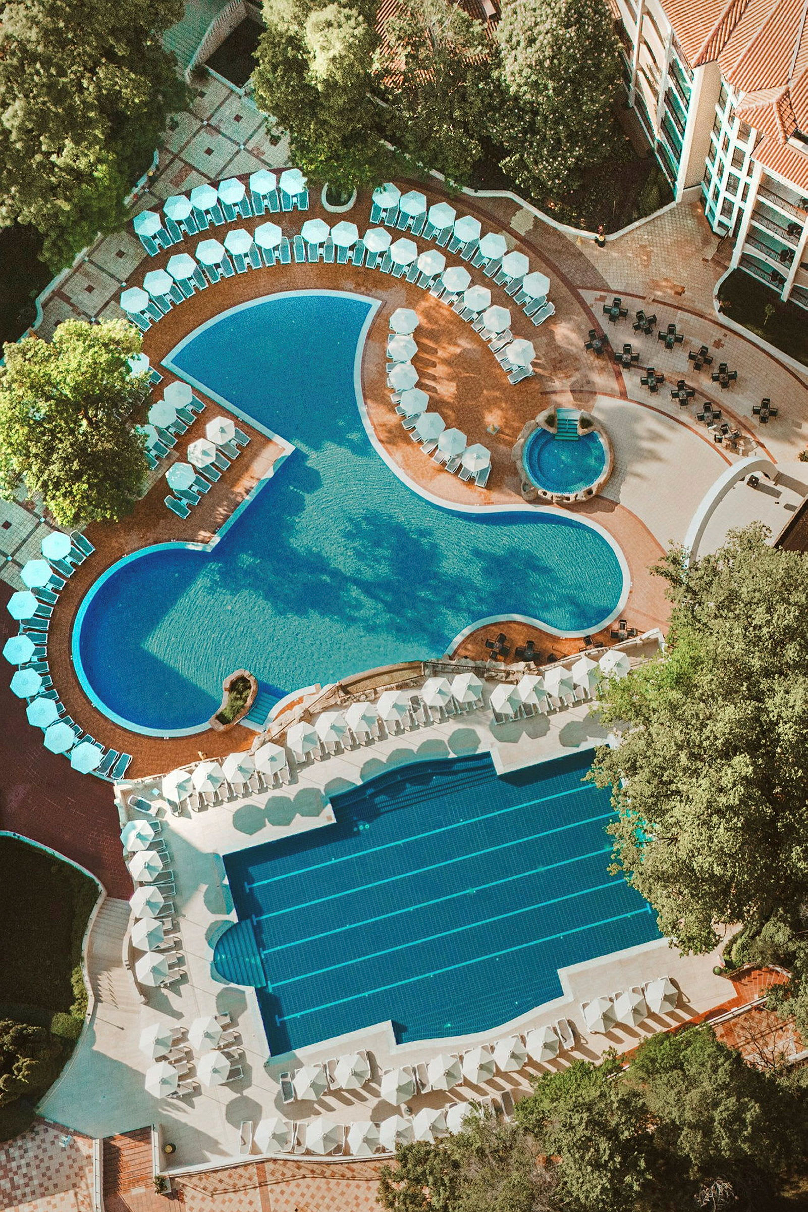Flygbild av en hotellpool med solstolar och parasoller runt omkring. (AI-genererad text)