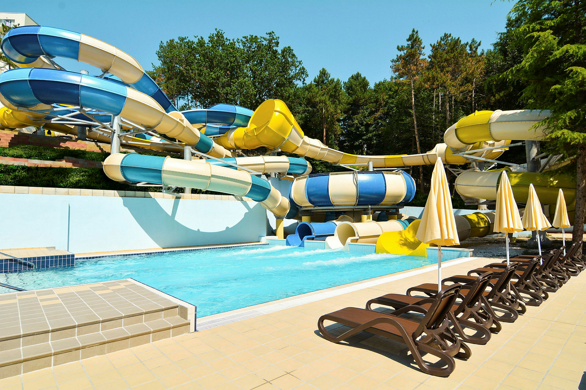 En pool med vattenrutschbanor och solsängar. (AI-genererad text)