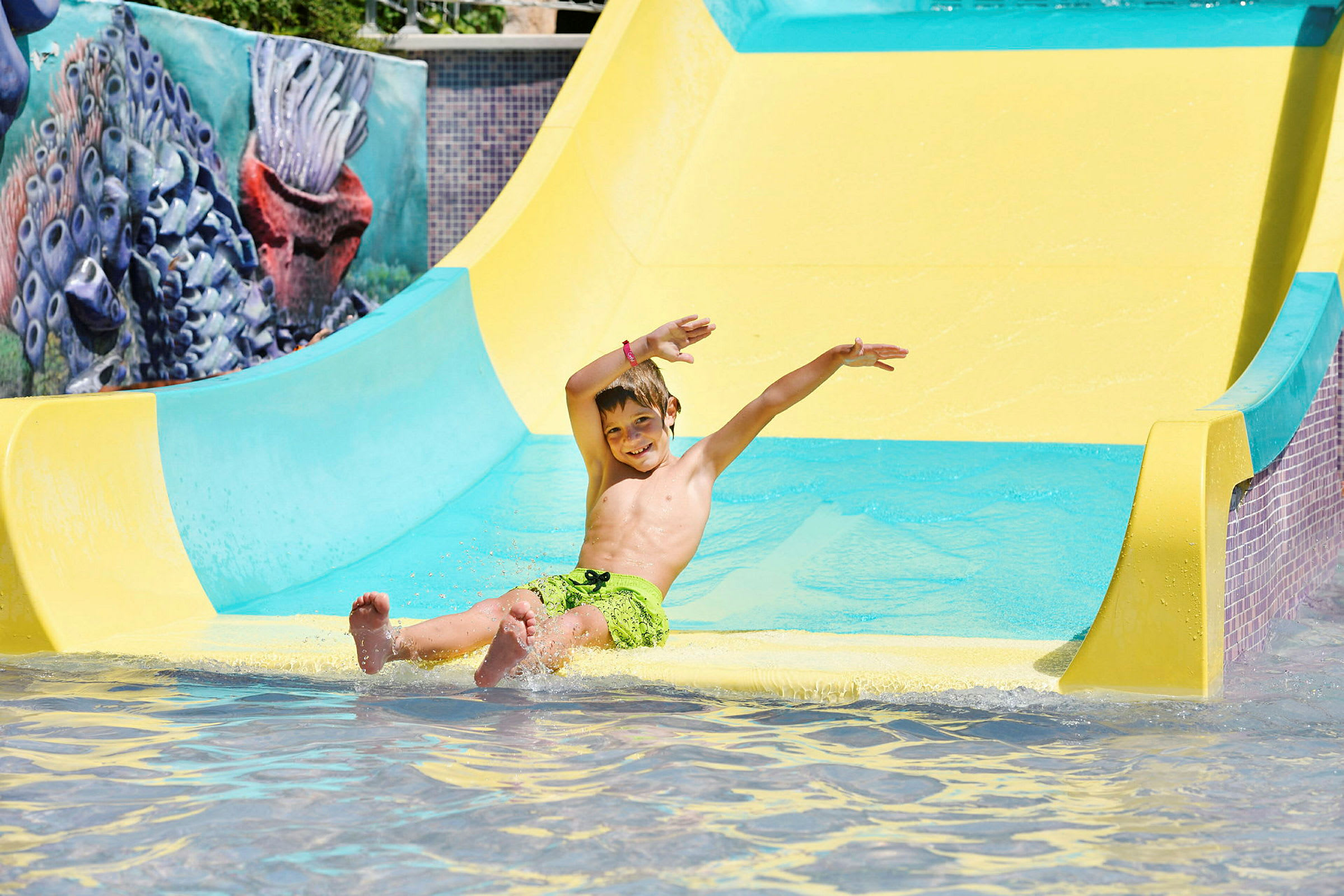 Ett barn glider nerför en gul vattenrutschkana och landar i en pool. (AI-genererad text)