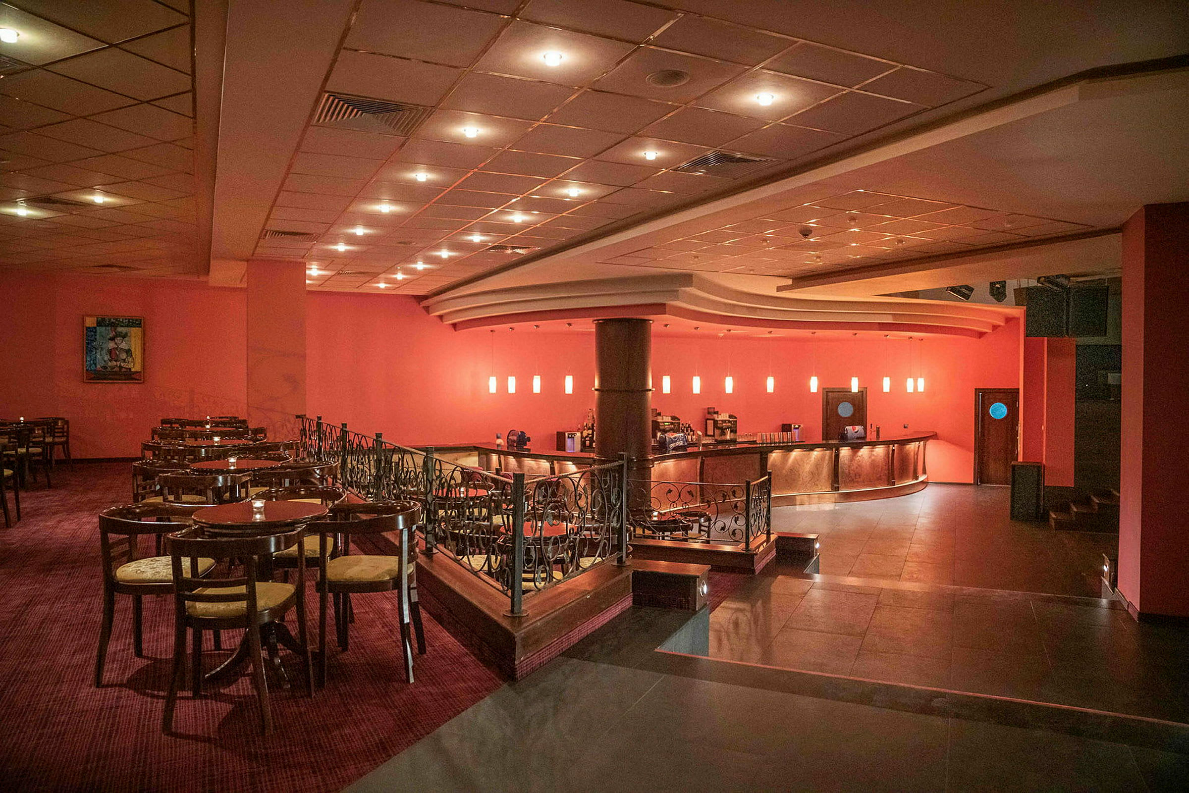 En restaurang med bord och stolar samt en bar med glödande lampor i bakgrunden. (AI-genererad text)