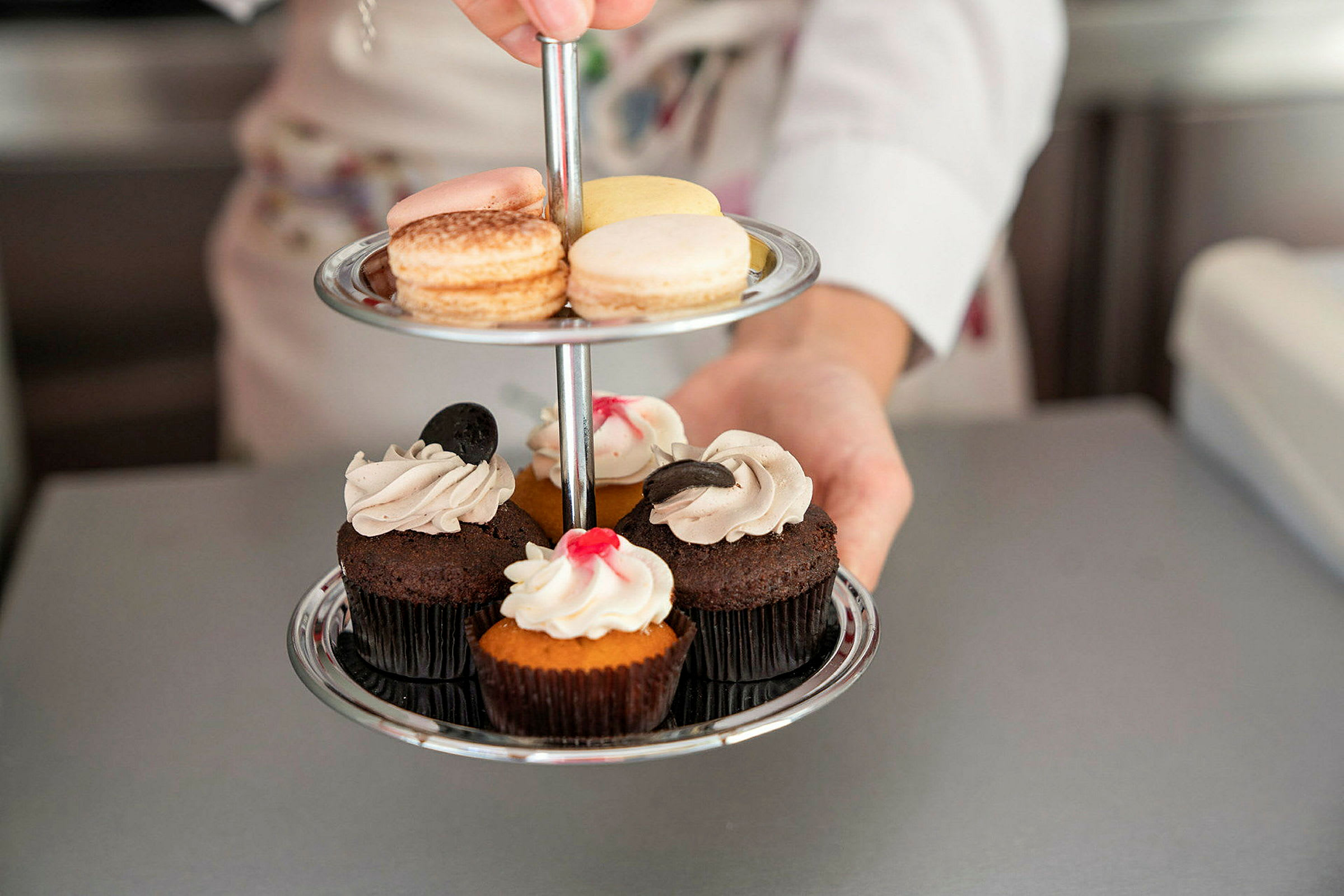 En person håller ett tvåvånings serveringsfat med macarons och muffins. (AI-genererad text)