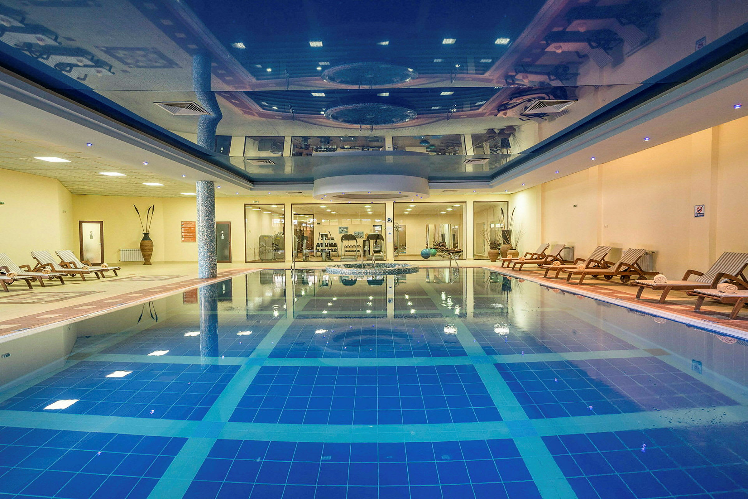 En inomhuspool med solstolar och träningsutrustning i bakgrunden. (AI-genererad text)