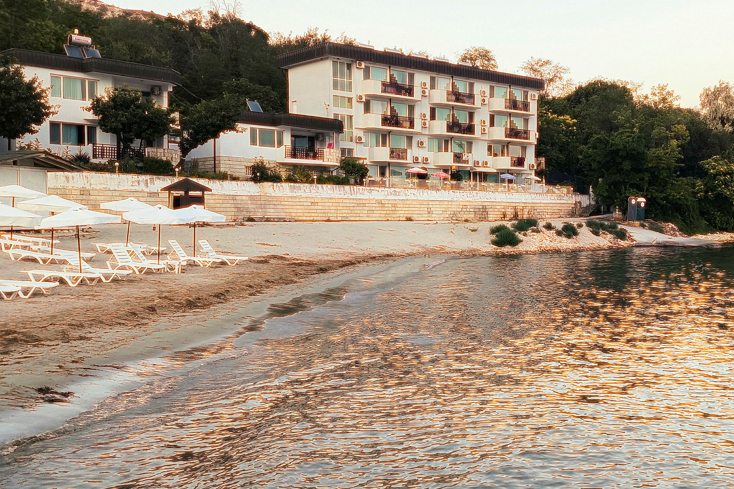 Strand med solstolar och parasoller framför en vit byggnad. (AI-genererad text)