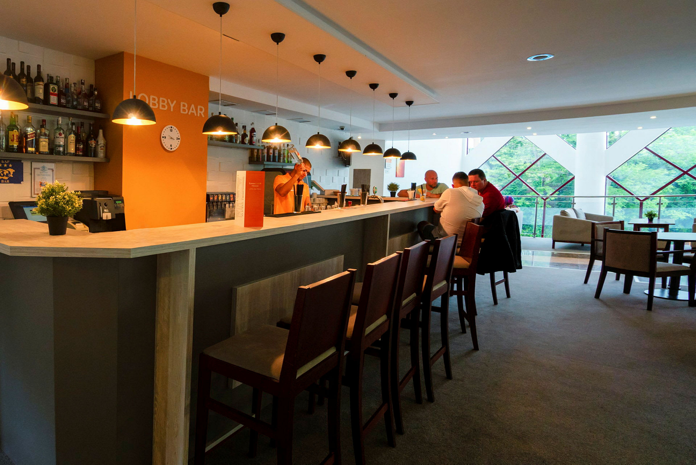 En lobbybar med belysning, stolar och människor som sitter vid disken. (AI-genererad text)