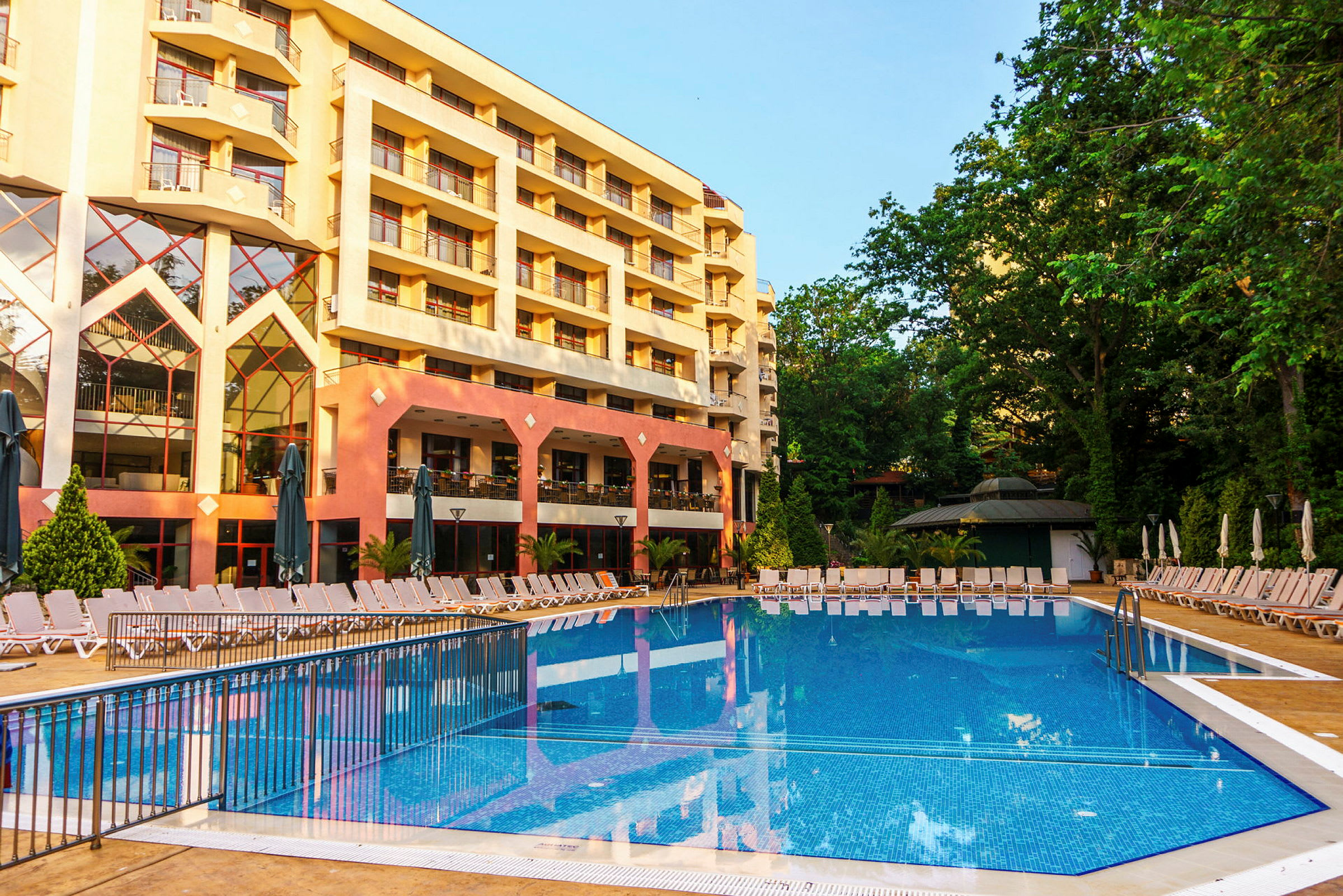 Hotellfasad med en pool och solstolar i förgrunden. (AI-genererad text)
