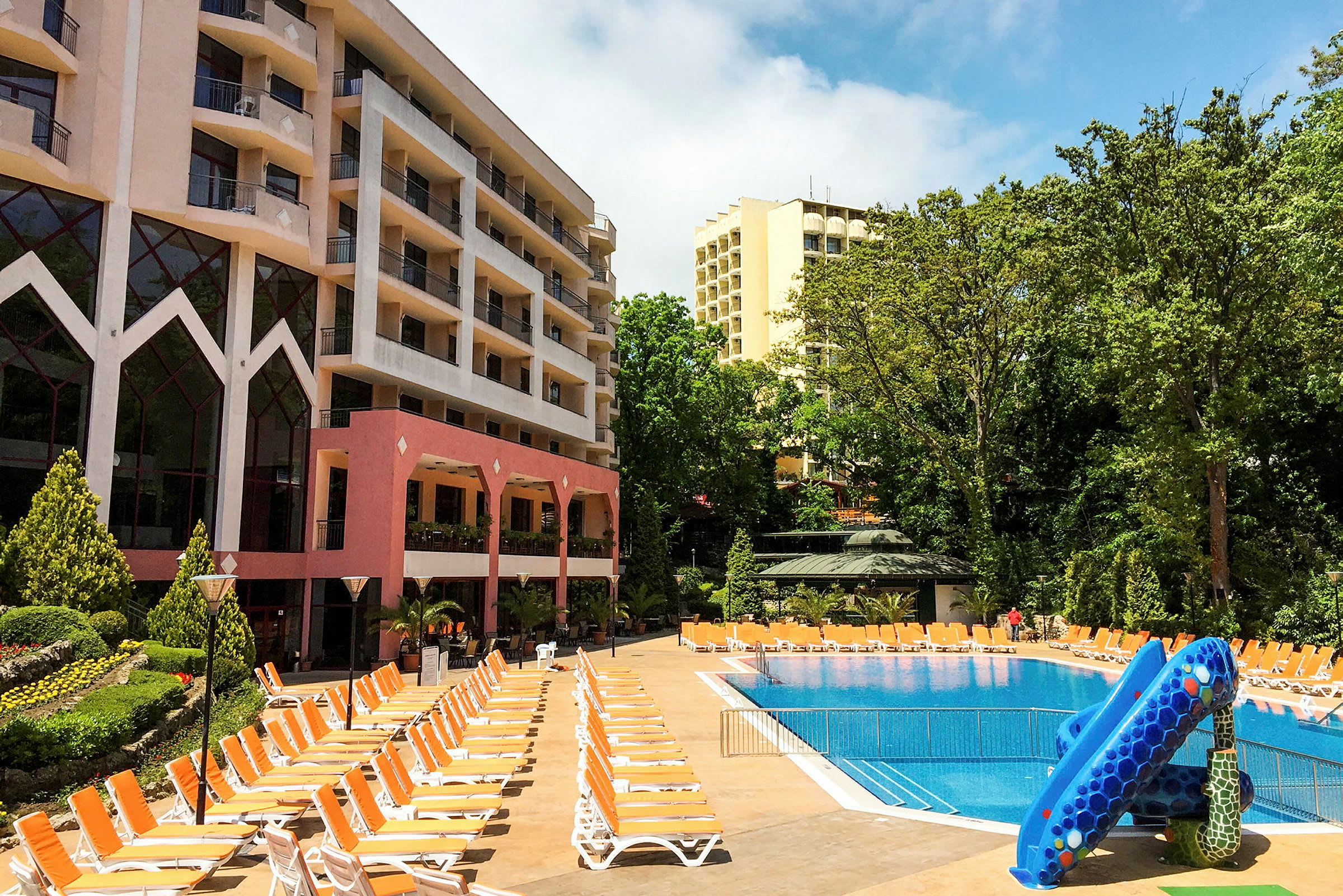 Hotellbyggnader vid en utomhuspool med solstolar och vattenrutschbana. (AI-genererad text)
