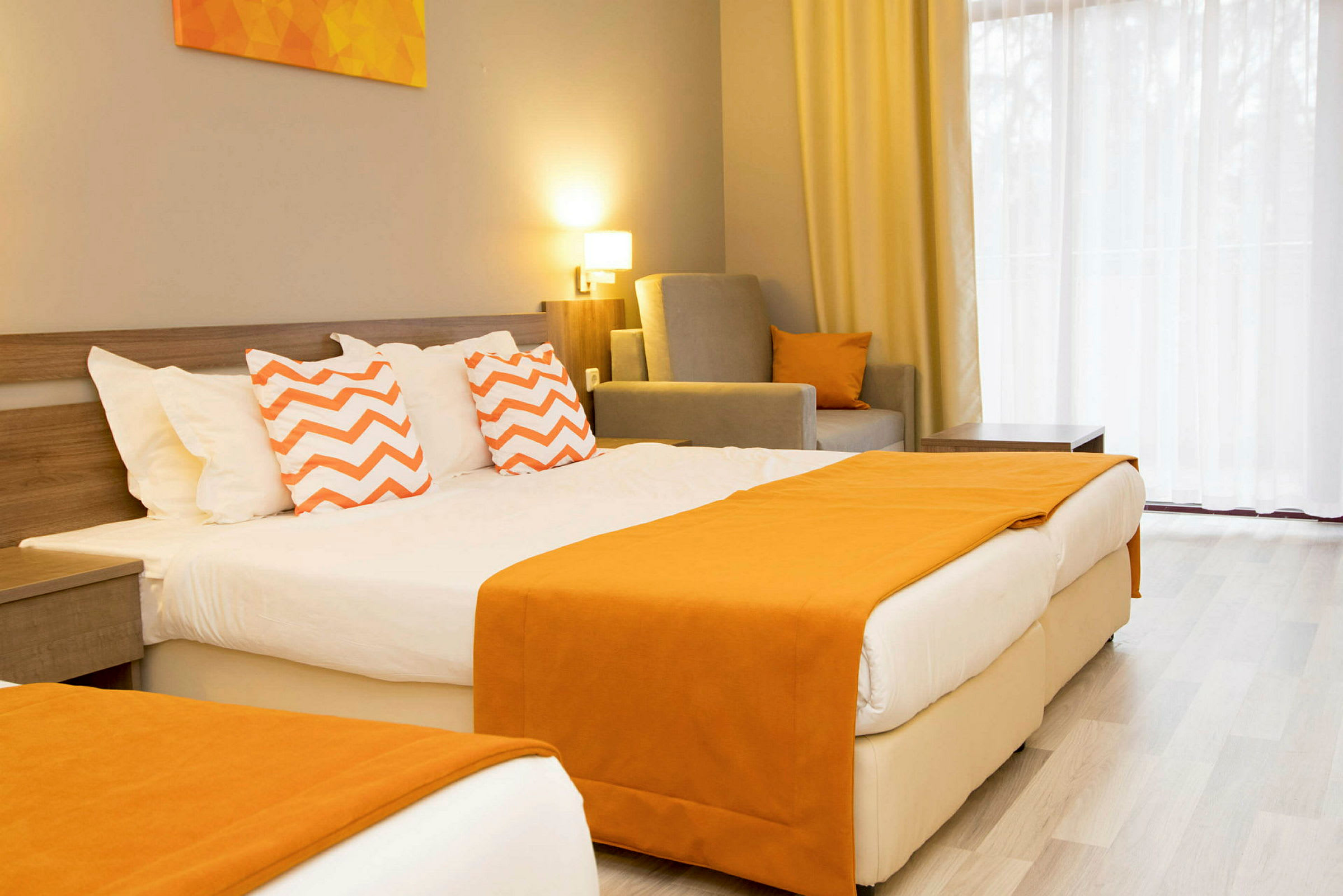 Hotellrum med en dubbelsäng, dekorerad med orange filtar och kuddar med zigzag-mönster. (AI-genererad text)