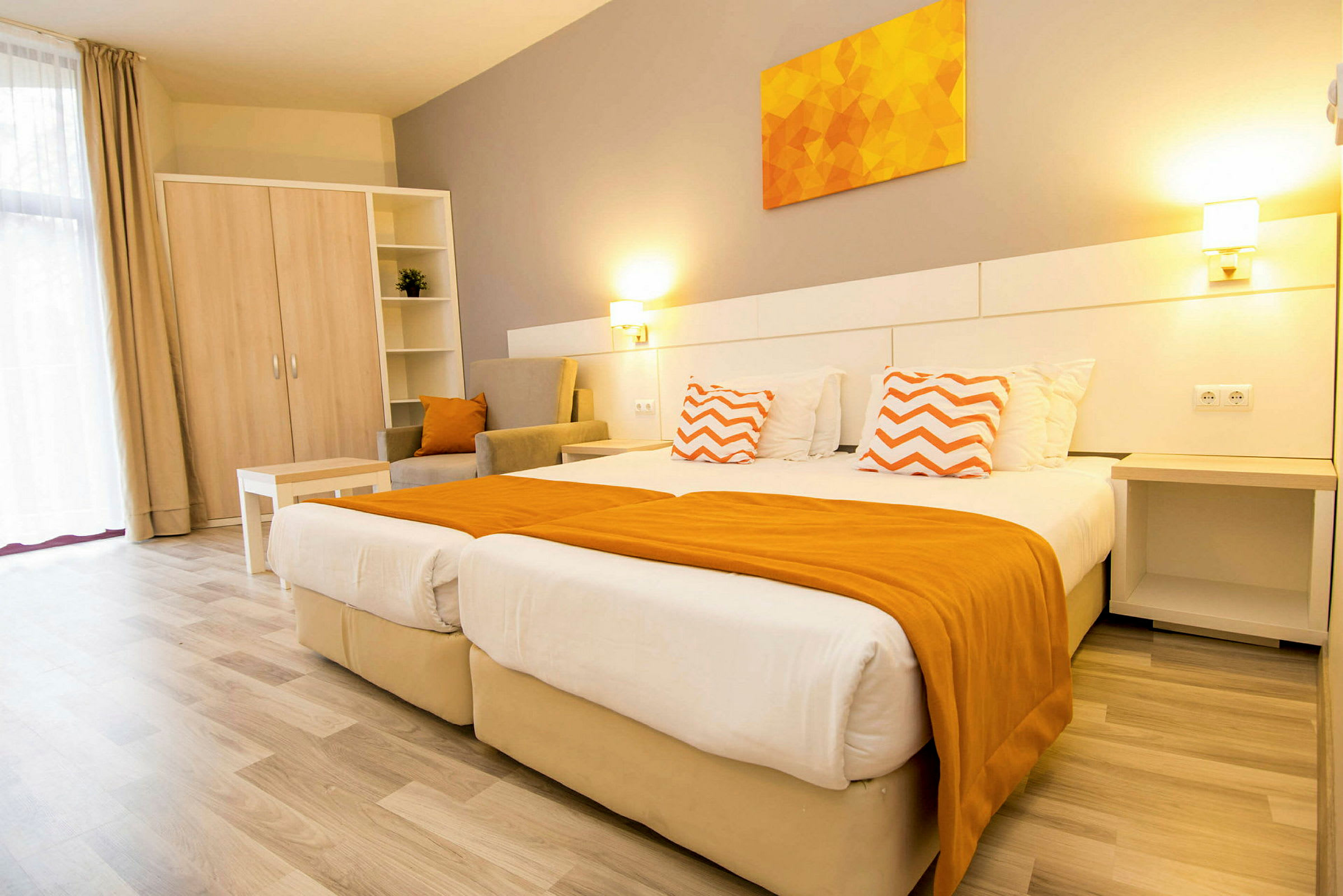 Ett ljust hotellrum med två sängar, orange detaljer och möbler. (AI-genererad text)