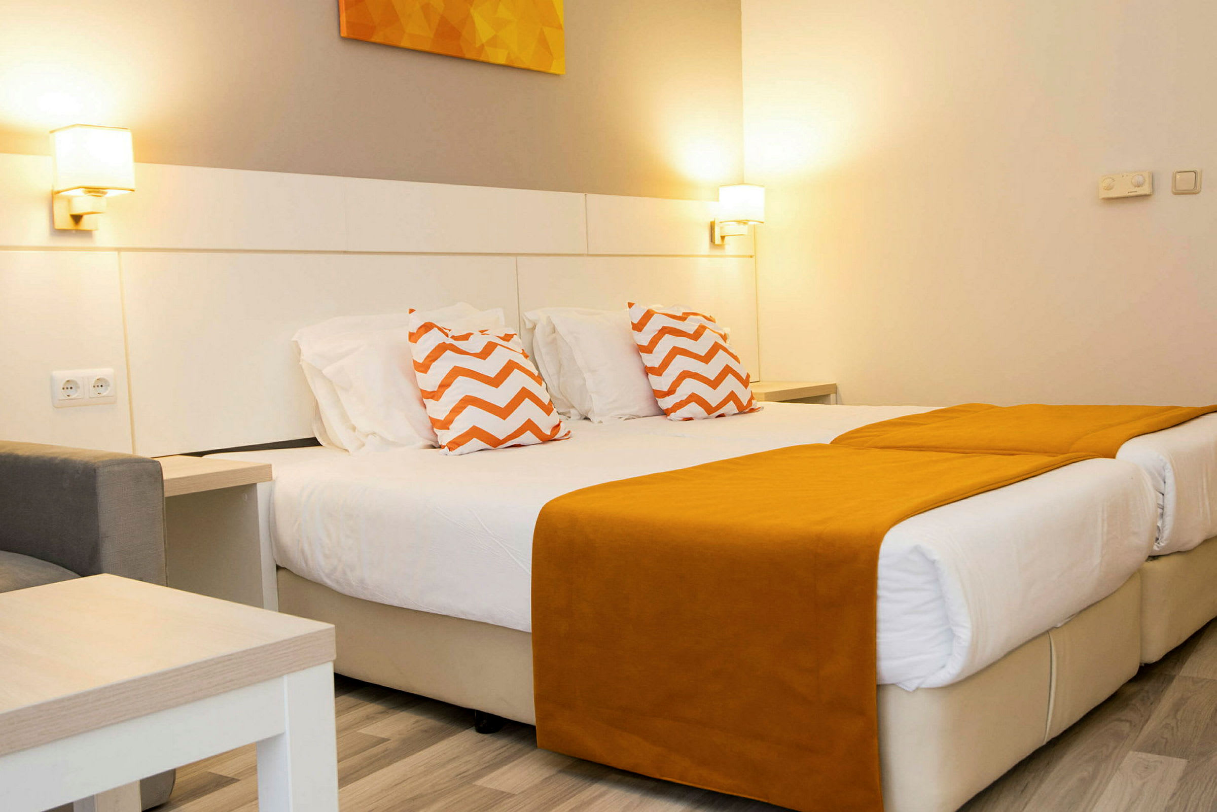 Ett hotellrum med två enkelsängar med orange sängöverdrag och prydnadskuddar med zigzag-mönster. (AI-genererad text)