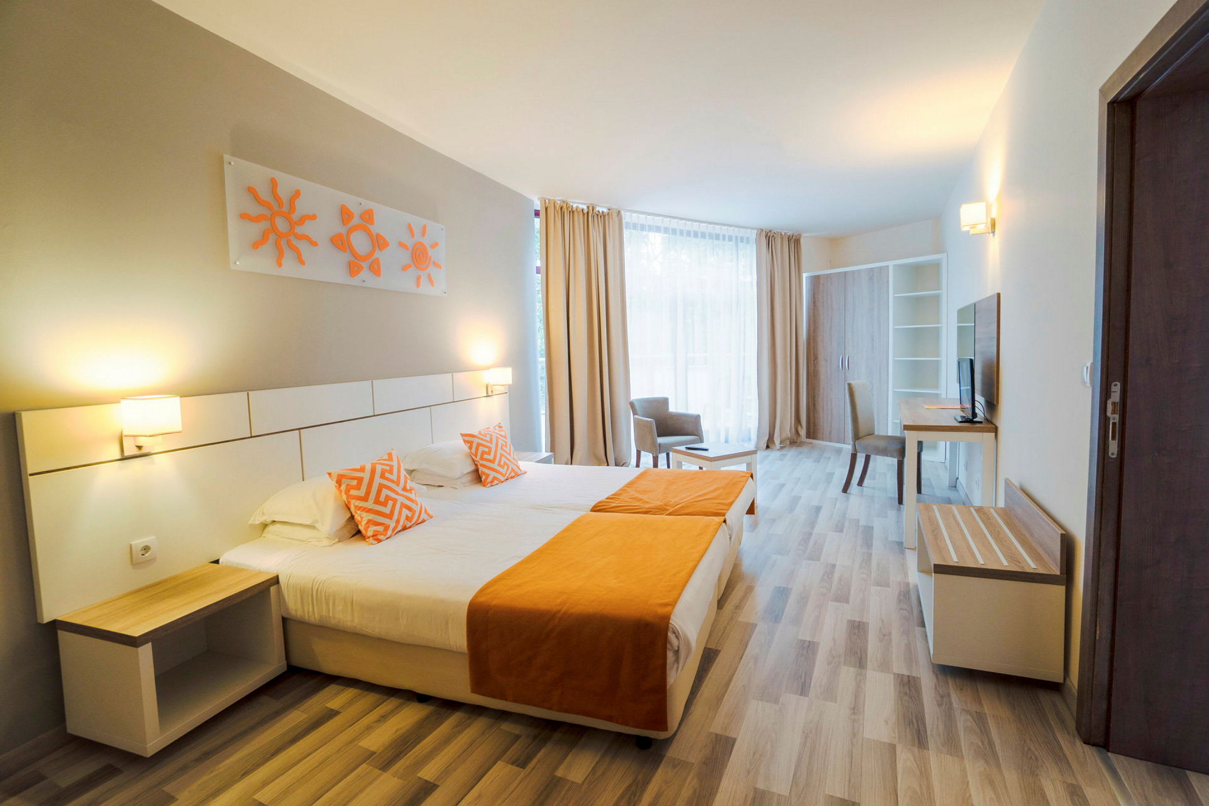 Ett hotellrum med en dubbelsäng som har orange detaljer, två sänglampor och modern inredning. En bred fönsteryta med ljusa gardiner syns i bakgrunden. (AI-genererad text)