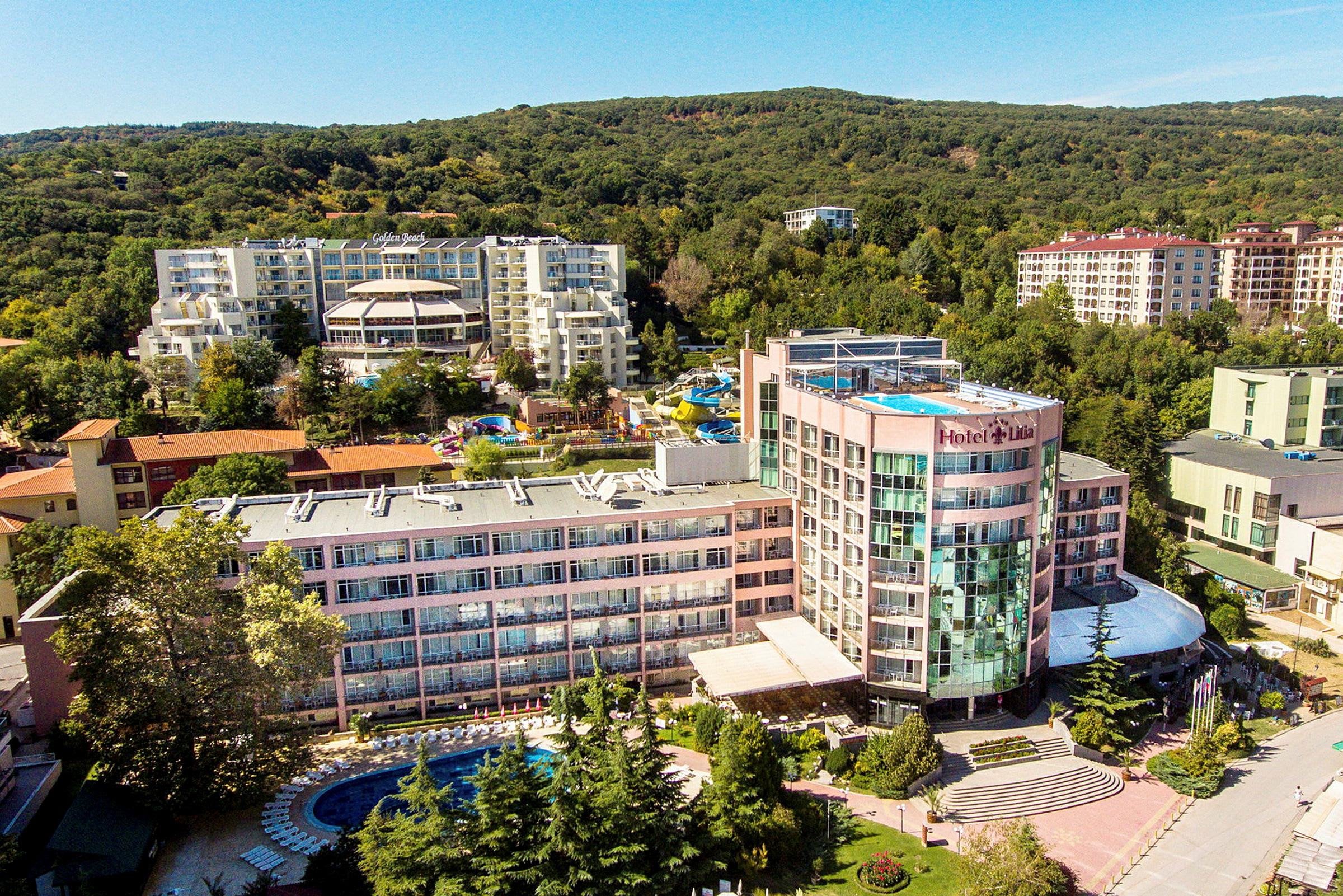 Vy över ett hotellkomplex med pool och omgivande grönska. (AI-genererad text)