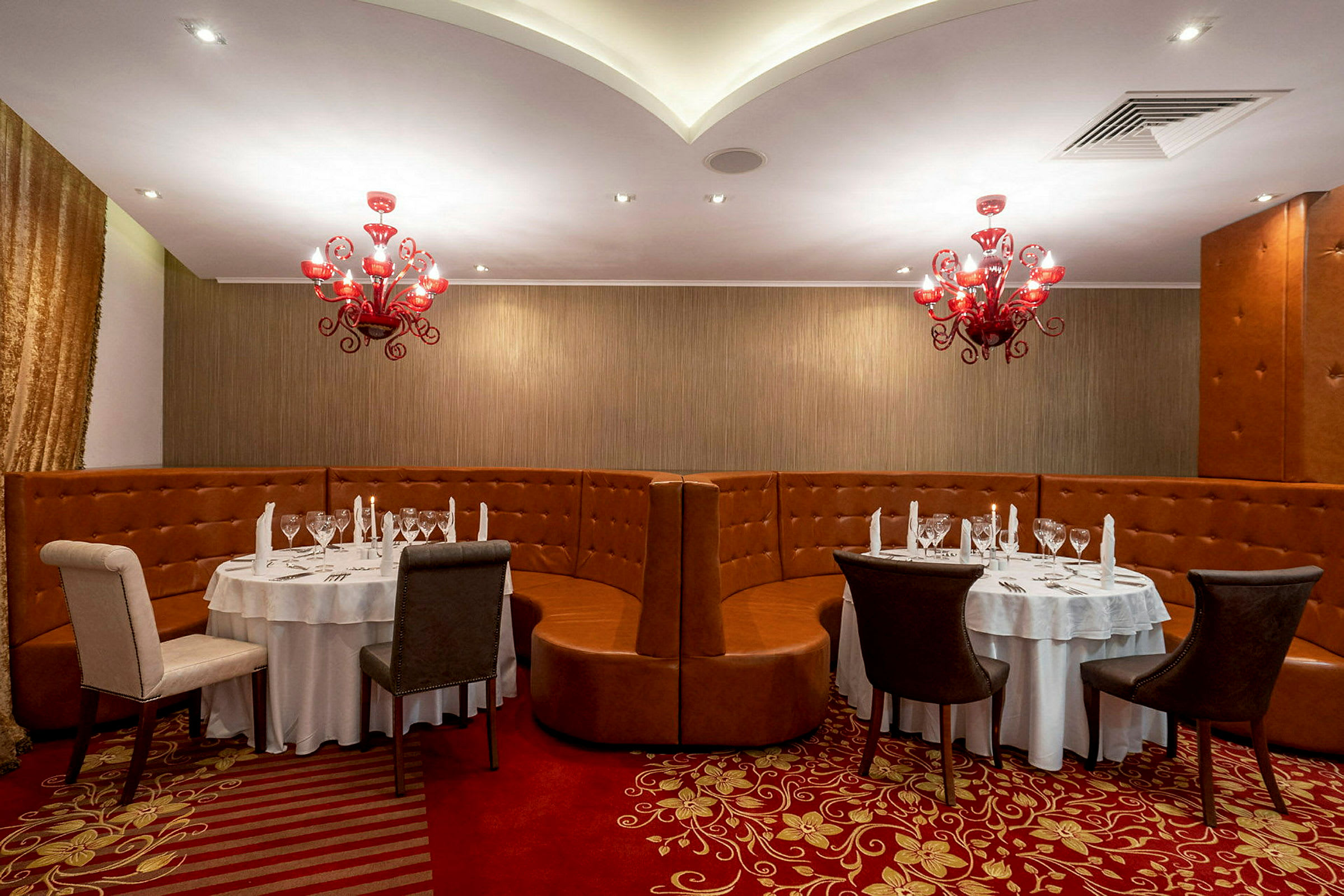 En restaurang med runda bord, stolar och röda ljuskronor. (AI-genererad text)