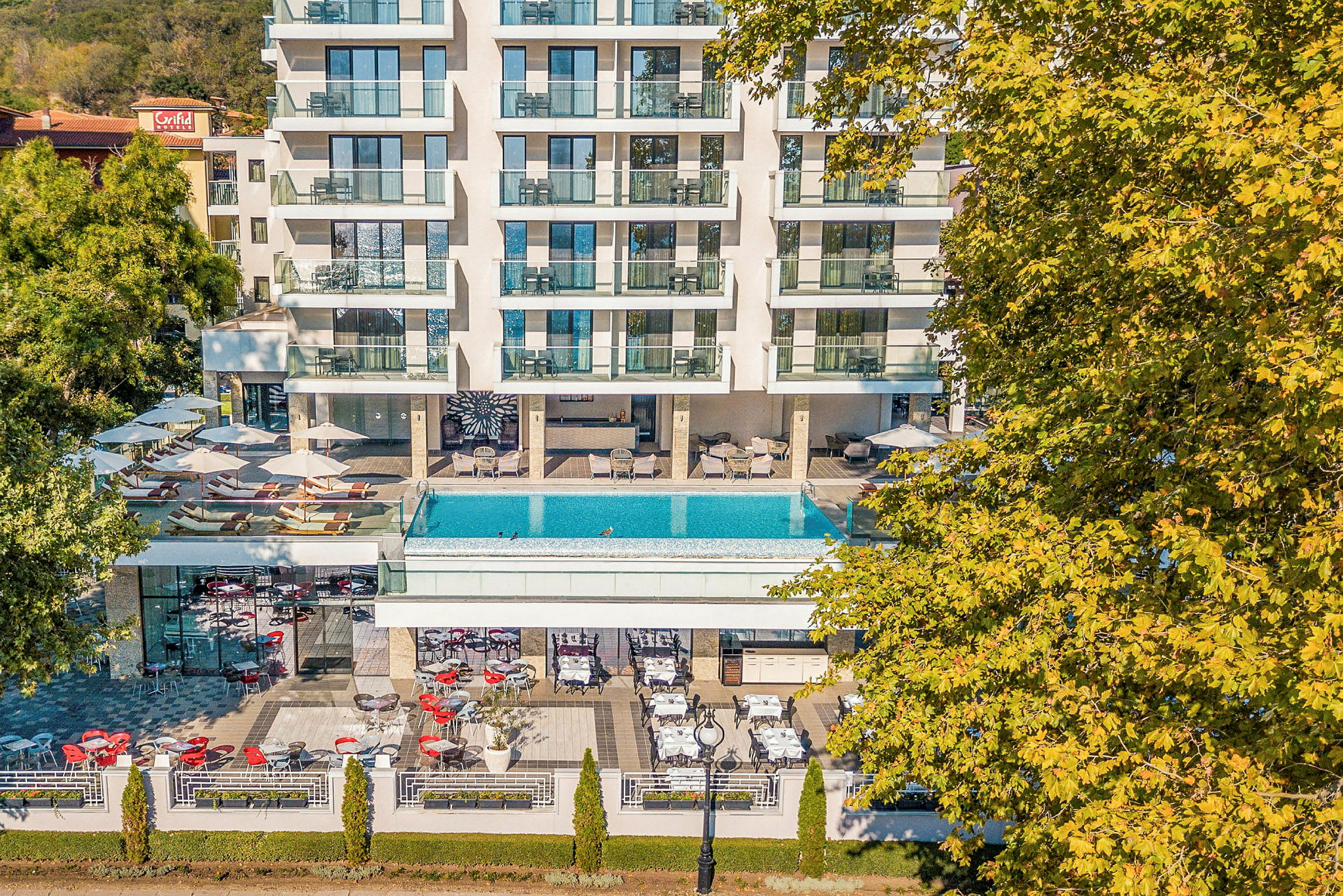 Hotell med balkonger, pool och utomhusservering omgivet av grönska. (AI-genererad text)