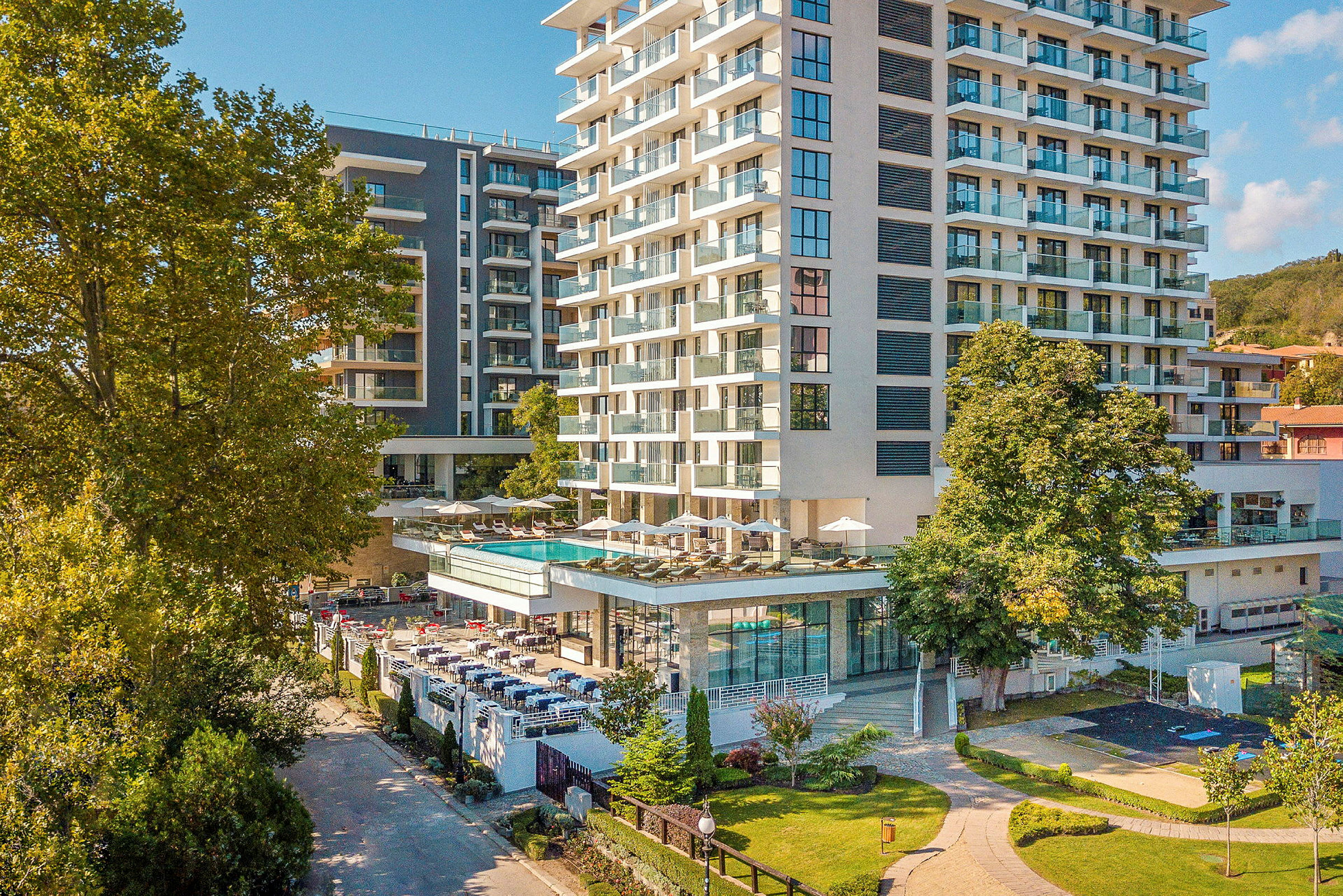 En hotellbyggnad med flera våningar omgiven av grönska, en utomhuspool och sittplatser syns. (AI-genererad text)