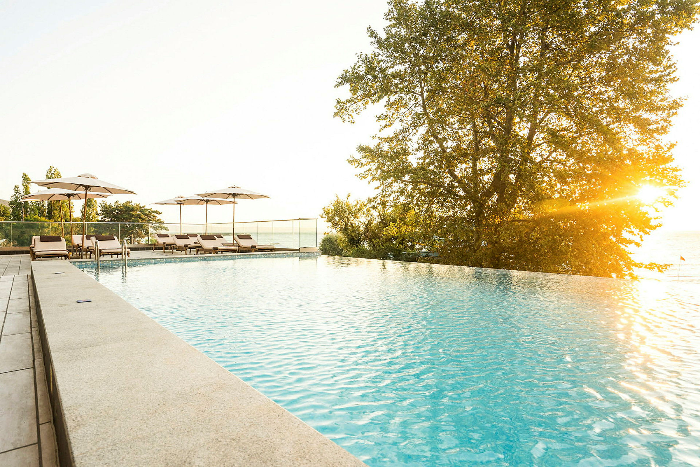 En infinitypool med solstolar och parasoller vid solnedgången. (AI-genererad text)