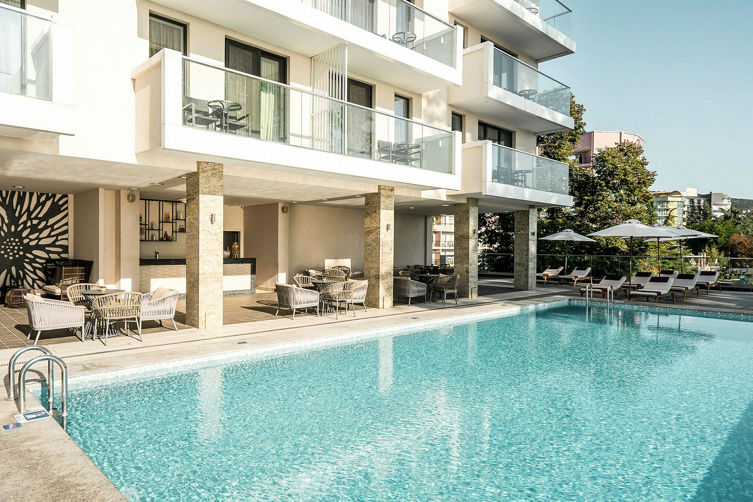 Exteriör av ett hotell med en utomhuspool, solstolar och sittgrupp. (AI-genererad text)