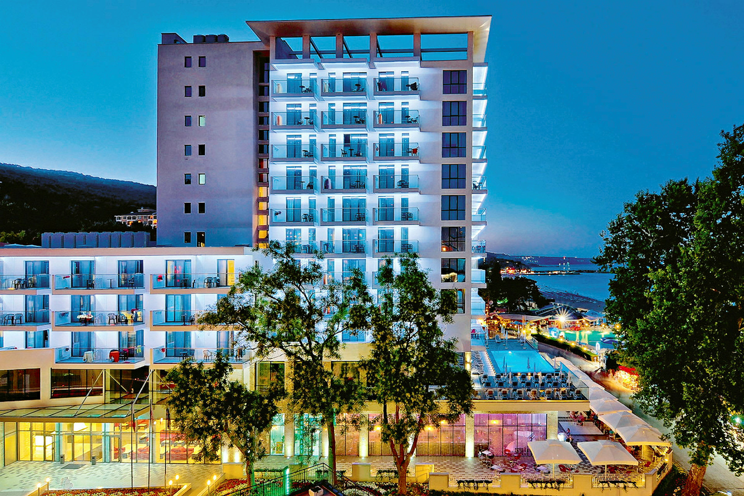 Modern hotellbyggnad upplyst på kvällen, med pool och omgivande grönska. (AI-genererad text)