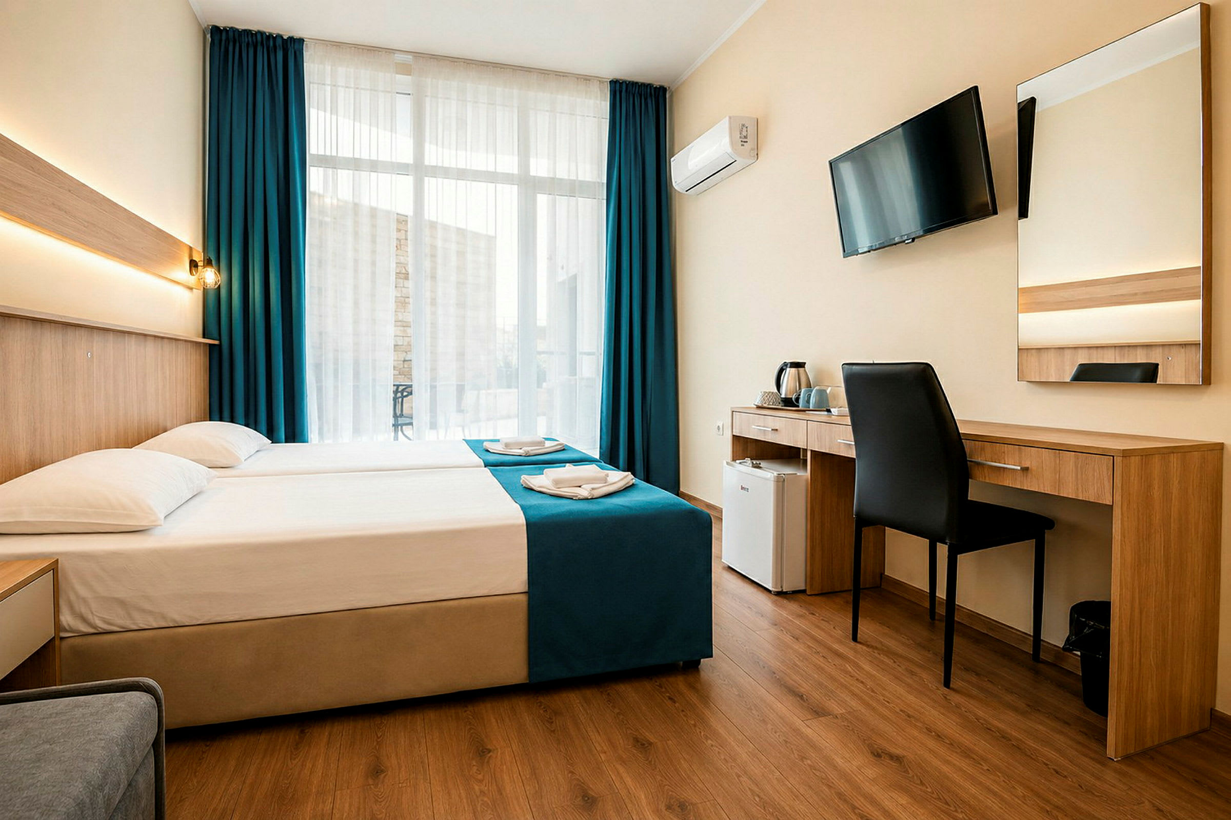 Ett hotellrum med en dubbelsäng, skrivbord, stol, väggmonterad TV och stora fönster med mörkblå gardiner. (AI-genererad text)