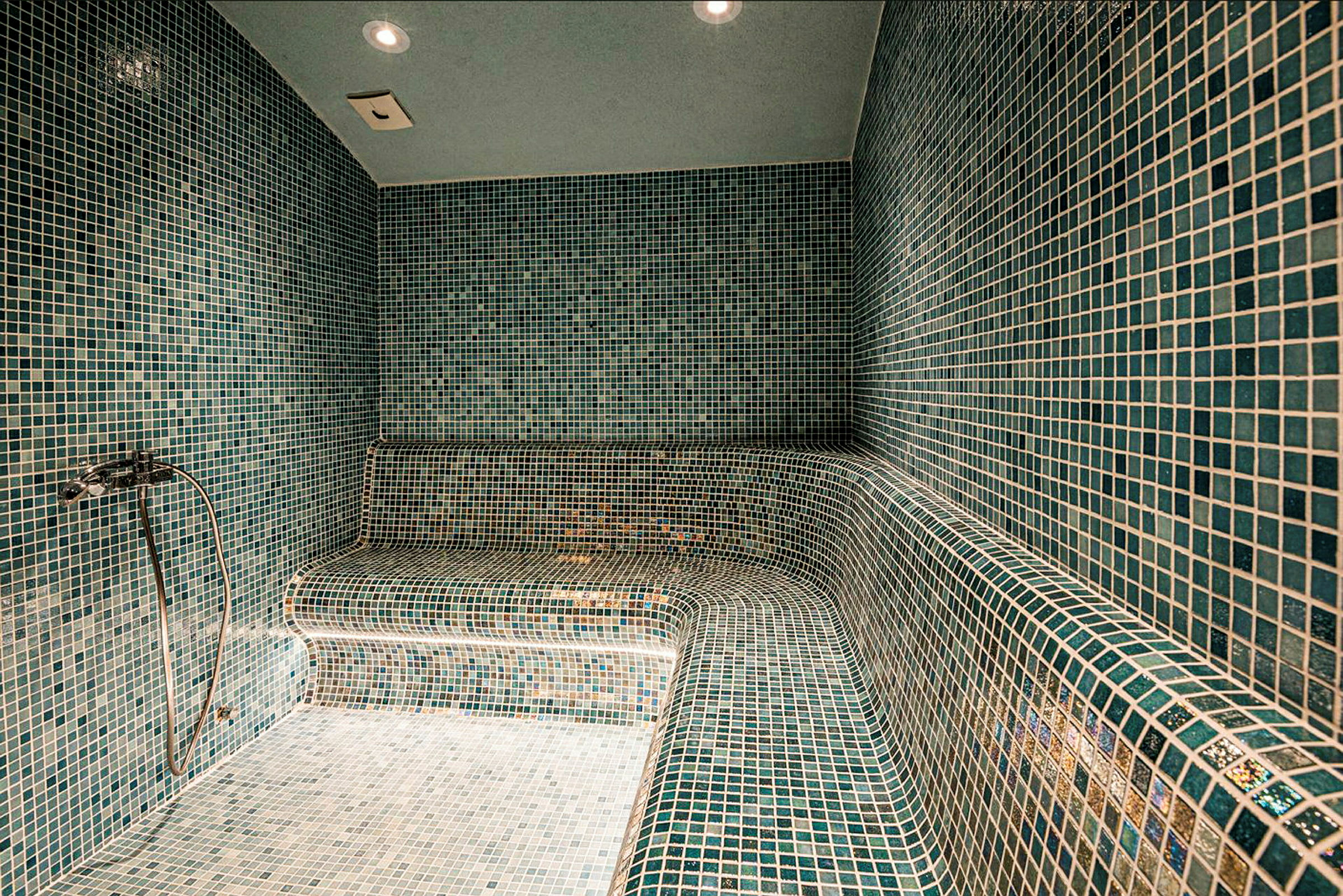 Ett ångbad med väggar, golv och sittbänkar täckta av gröna mosaikkakelplattor. (AI-genererad text)