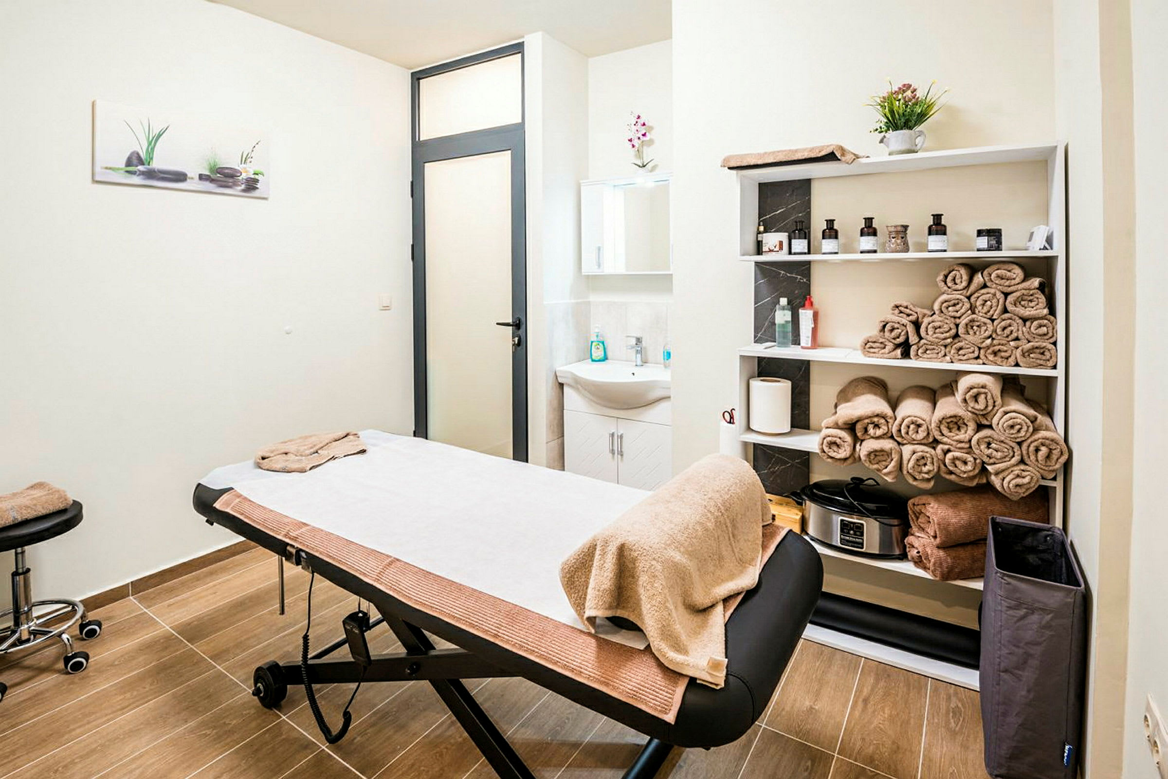 Ett massage- eller behandlingsrum med behandlingsbrits, handdukar på hyllor och diskbänk. (AI-genererad text)
