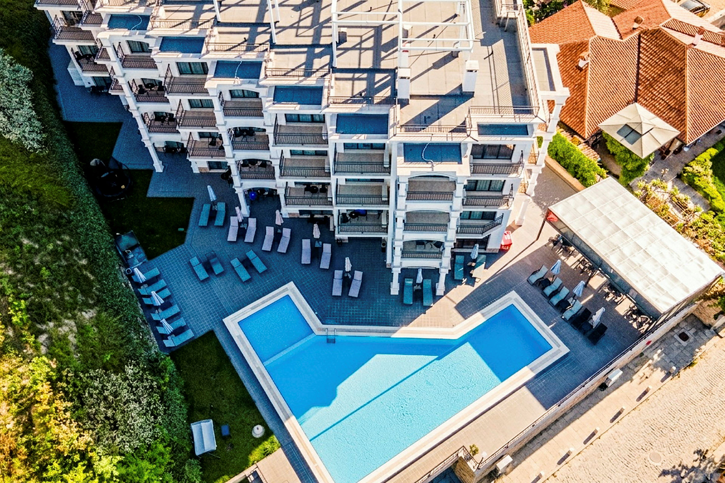 Flygfoto över en hotelbyggnad med en pool och solstolar utomhus. (AI-genererad text)