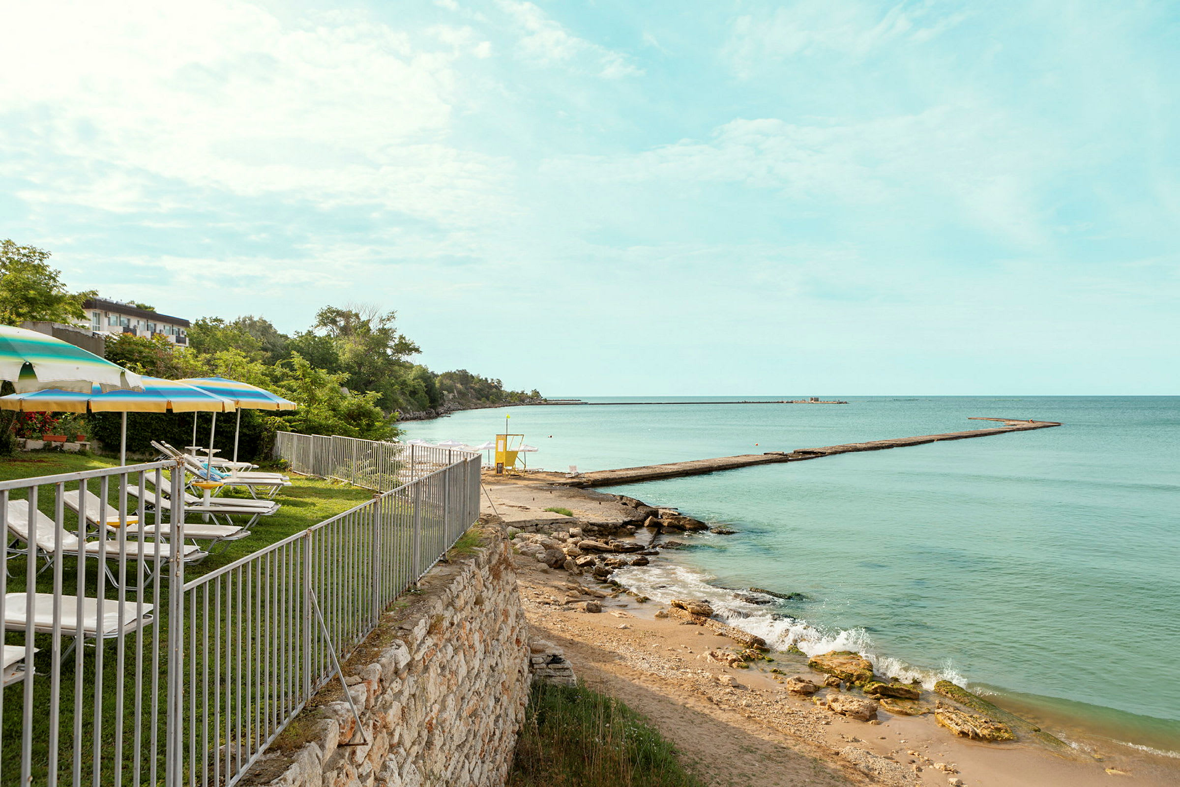 En strand med solstolar och parasoller vid ett staket nära havet. (AI-genererad text)