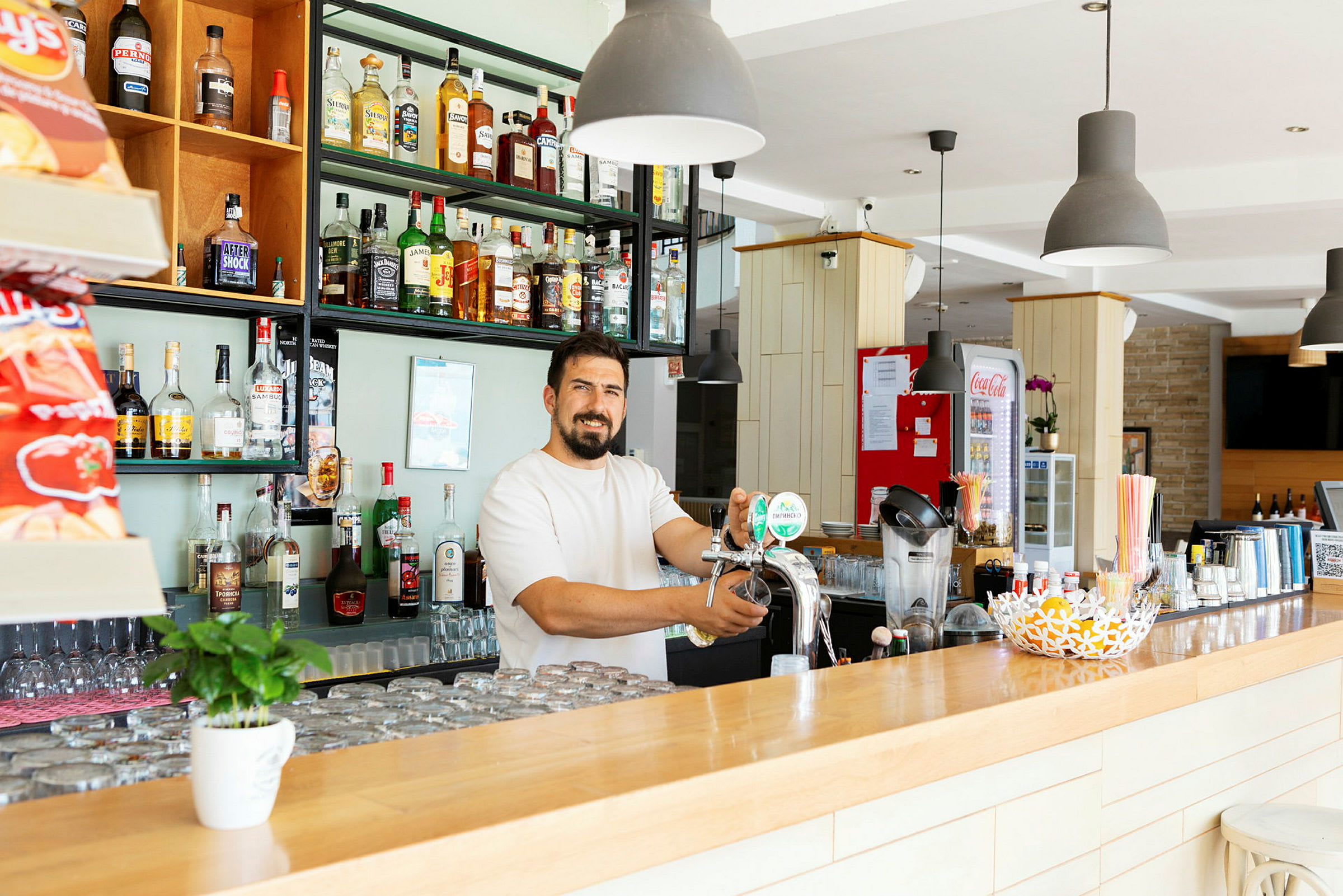 En bar med hyllor fyllda av flaskor och en person som tappar öl från en kran. (AI-genererad text)