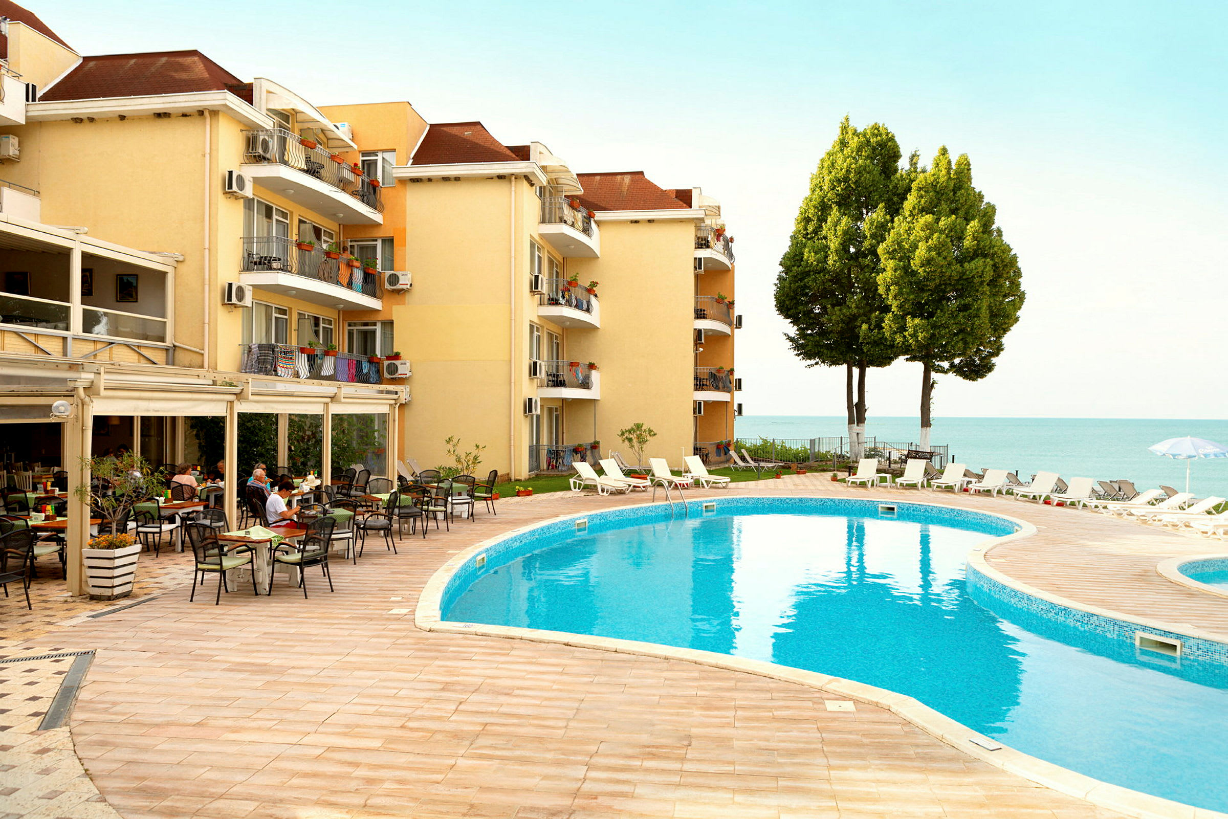 Hotellbyggnad vid en pool med solstolar och utsikt mot havet. (AI-genererad text)