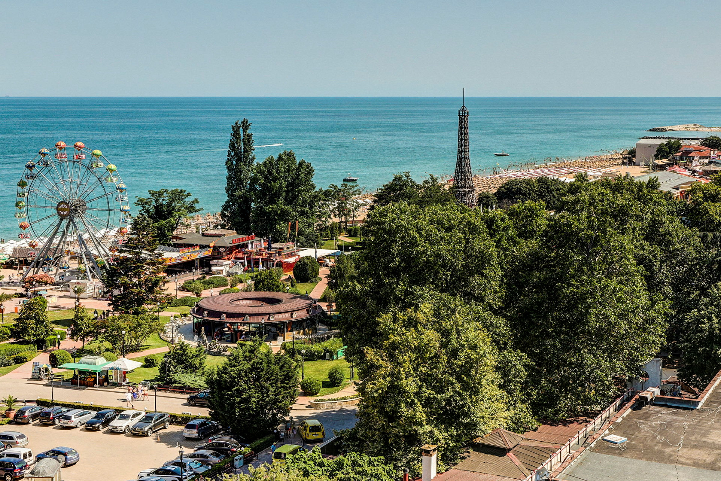 Utsikt över ett nöjesfält och en strand vid havet, med ett stort pariserhjul och grönområden. (AI-genererad text)